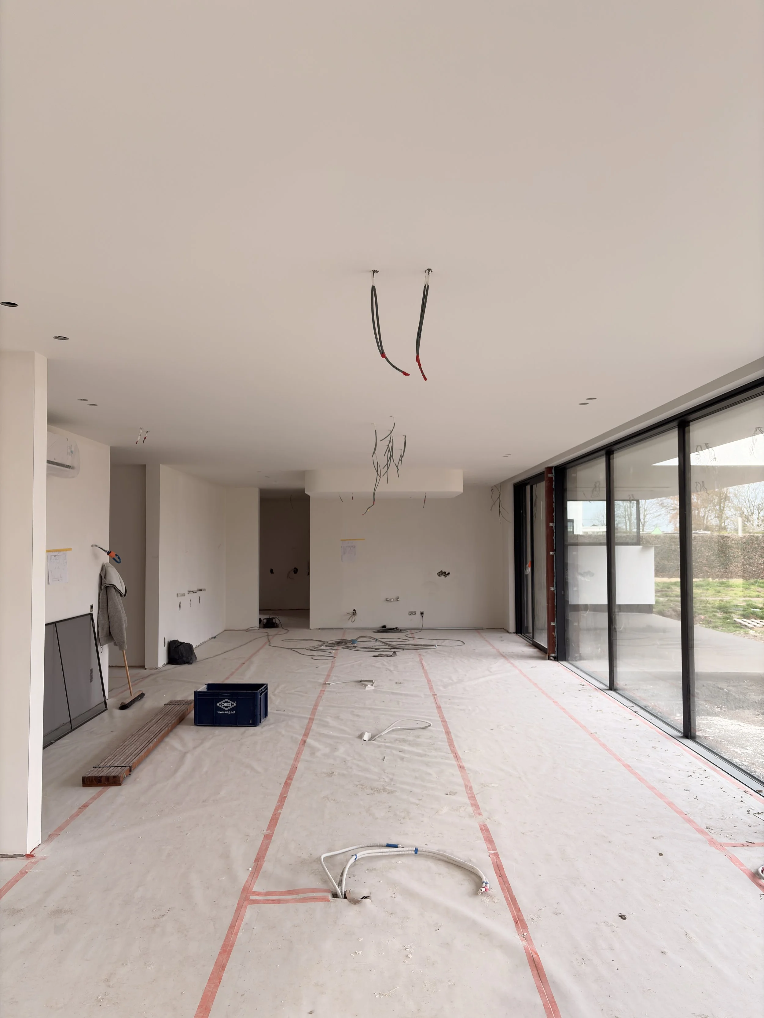 Interior of a room under construction with exposed wiring, construction materials, and large glass windows on the right.