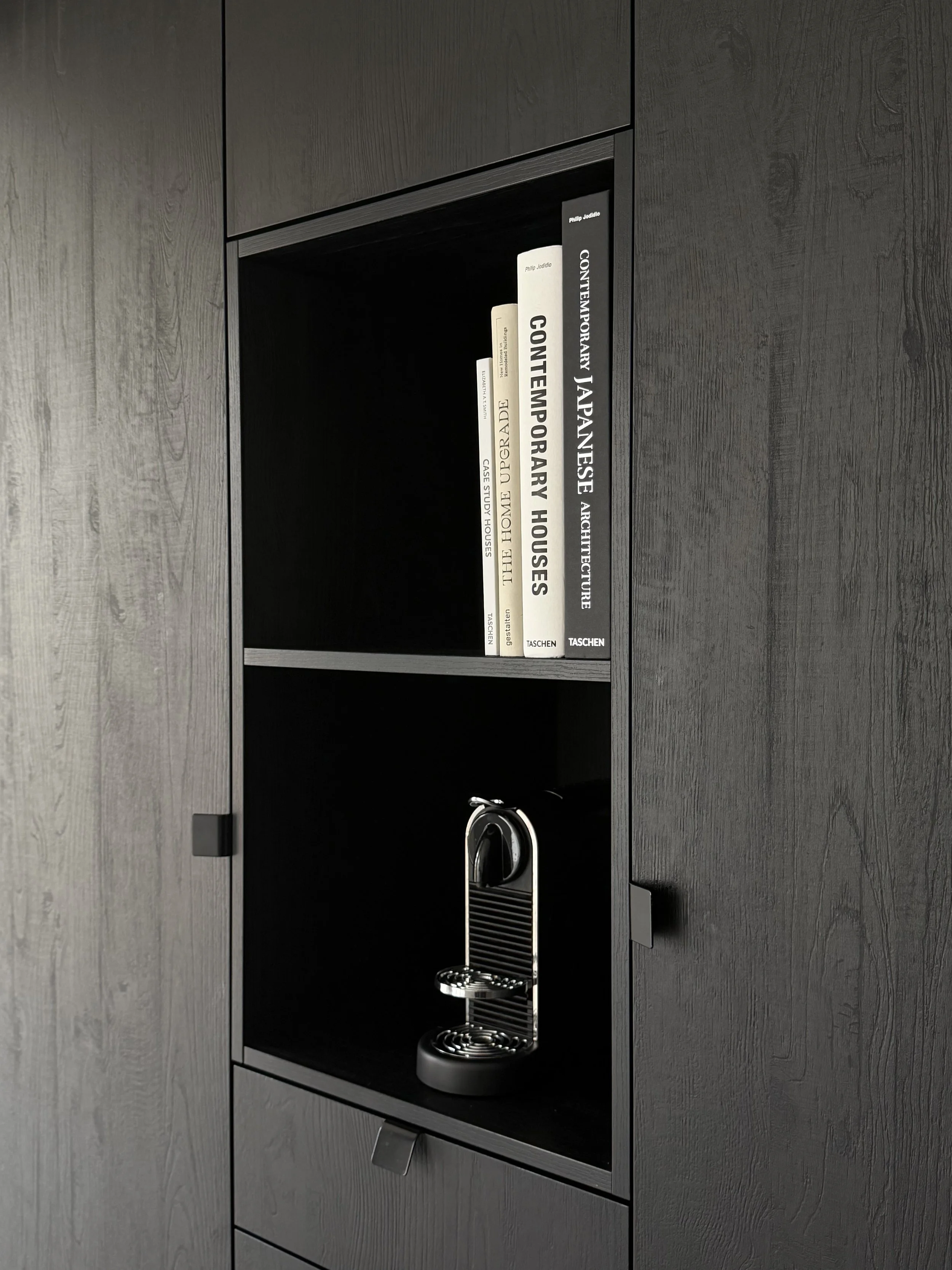 Een zwarte kast met een koffiezetapparaat en boeken over architectuur en interieurdesign.