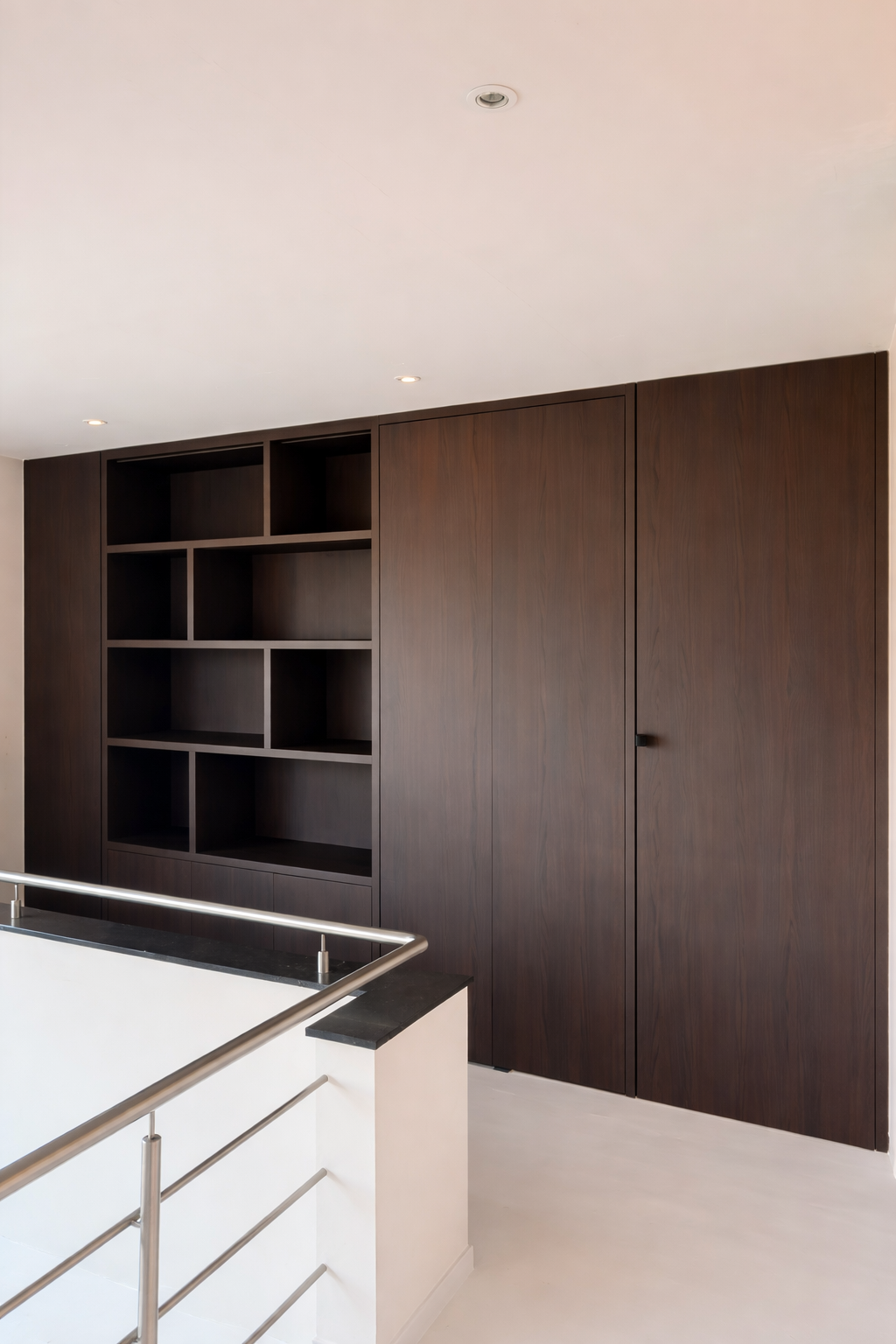 Modern interior with dark wooden wall unit and built-in shelves next to a staircase with metal railing.
