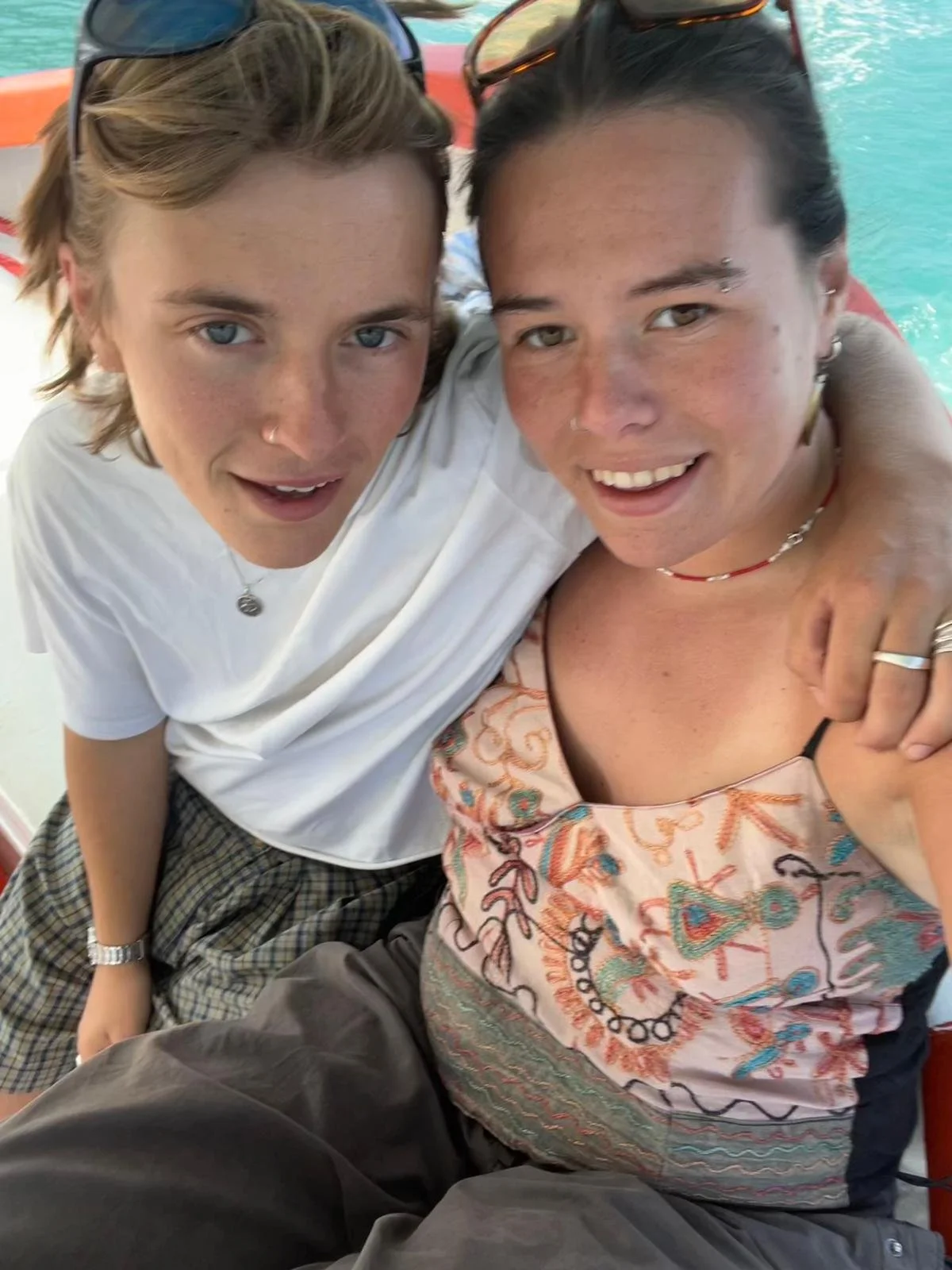 Two people taking a close-up selfie together near a swimming pool, smiling and wearing sunglasses.