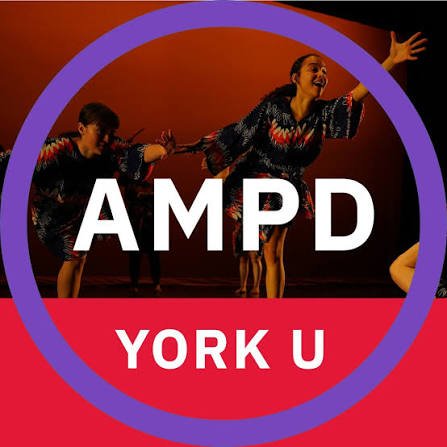 Two women dancing on stage with a large logo in front that reads 'AMPD YORK U' and a purple circle surrounding the logo.