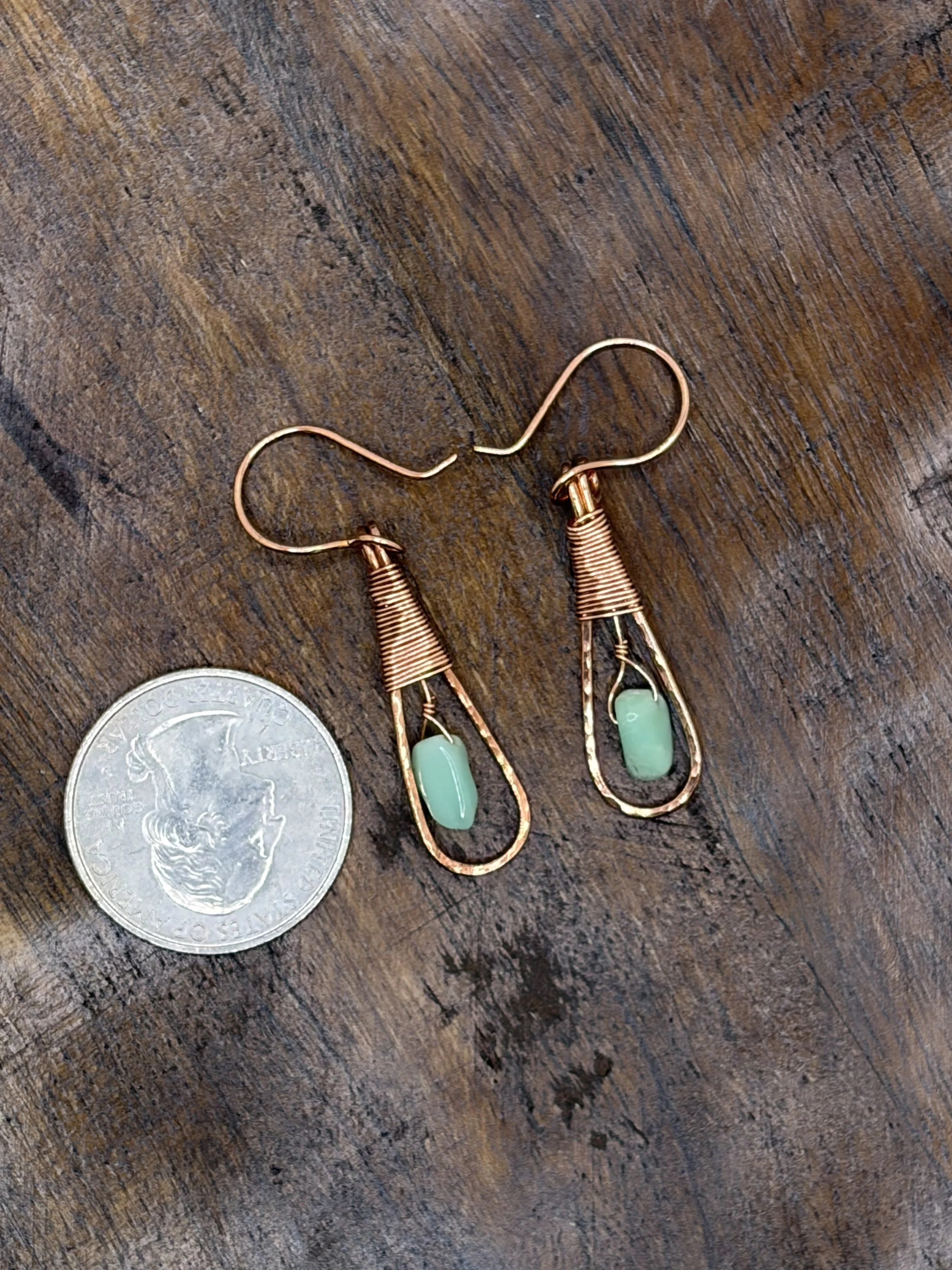 Pair of handmade hammered copper teardrop earrings with coiled wire caps and mint-green chrysoprase beads hanging from a gold display stand