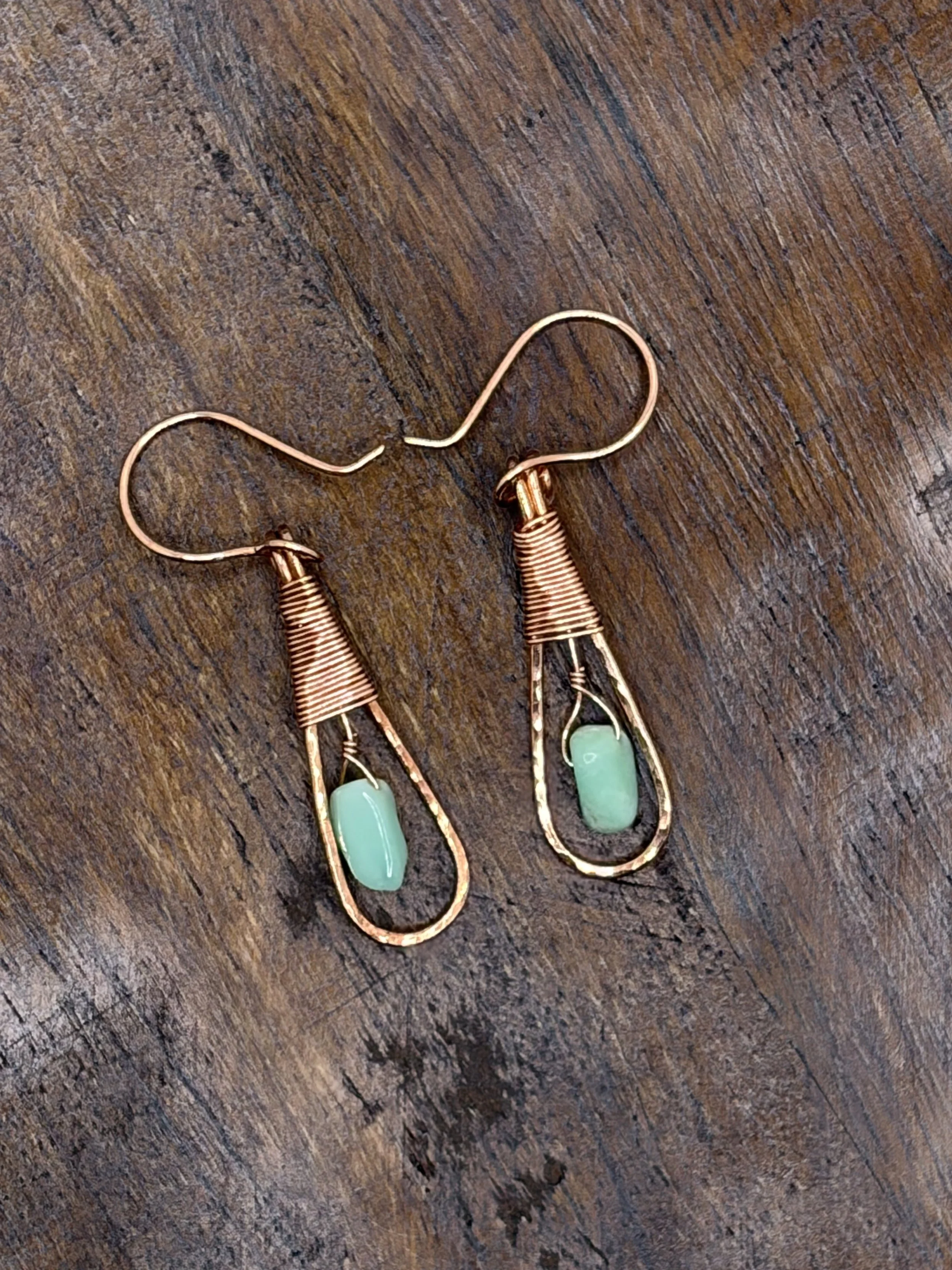 Pair of handmade hammered copper teardrop earrings with coiled wire caps and mint-green chrysoprase beads hanging from a gold display stand
