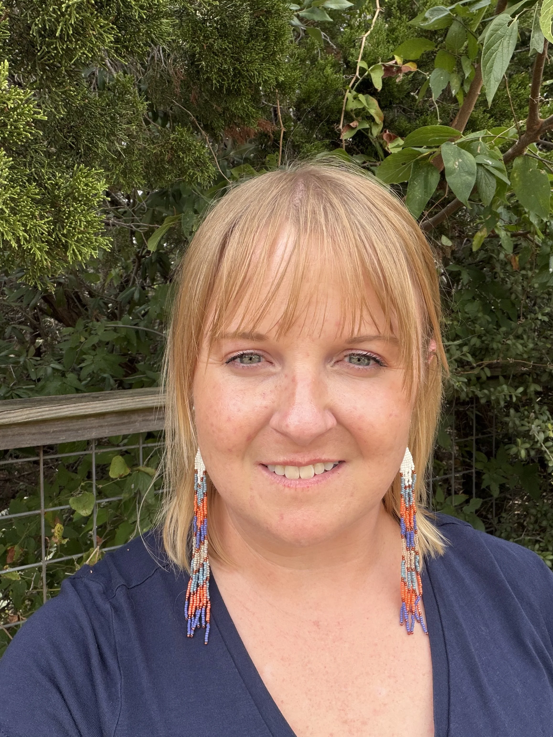 woman wearing handmade seed bead fringe earrings, cream slate blue orange purple and copper, gold ear wire