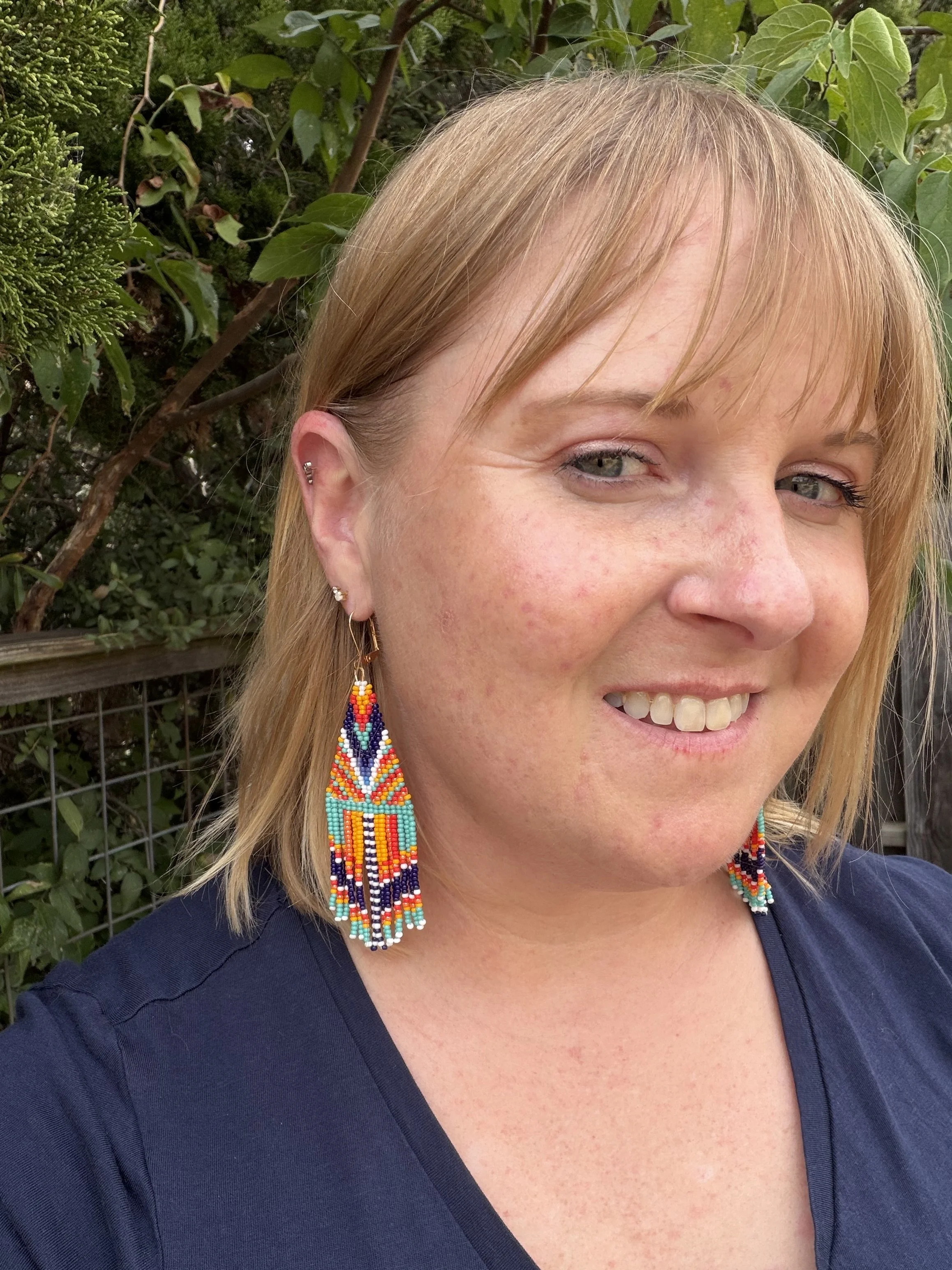Woman wearing handmade geometric seed bead fringe earrings, turquoise coral marigold navy and white, gold ear wire