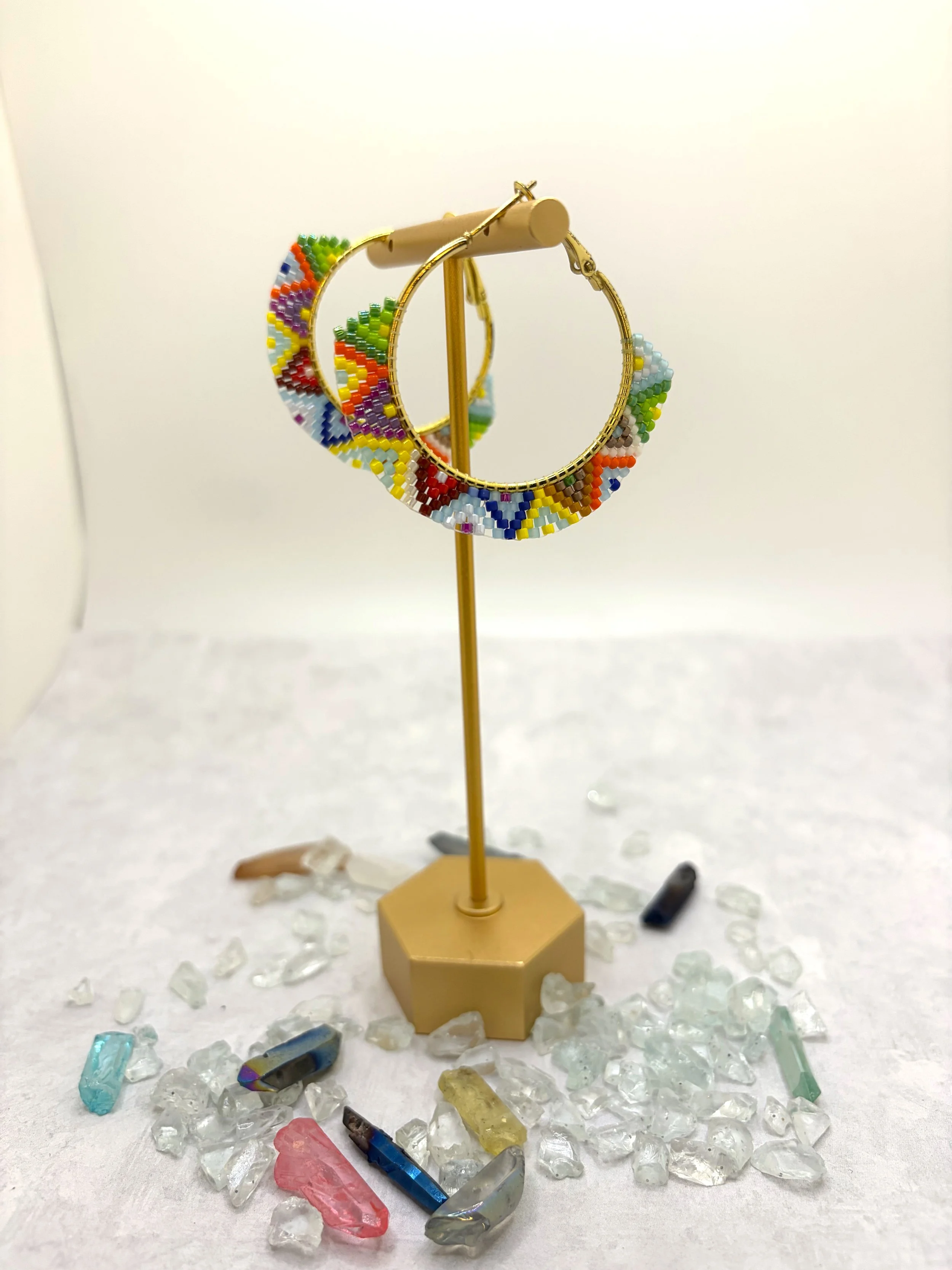 Multicolor seed bead woven hoop earrings in gold-tone metal with a geometric rainbow pattern.