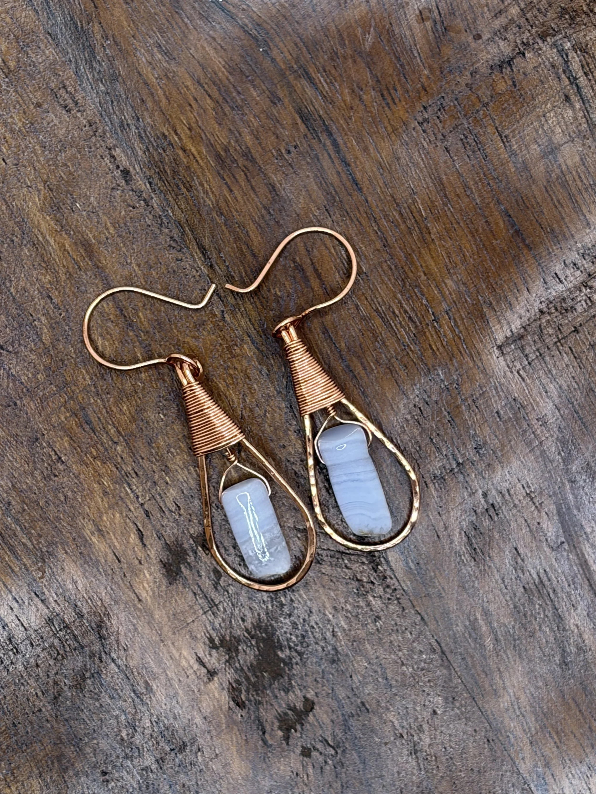 Pair of handmade hammered copper teardrop earrings with coiled wire caps and pale blue lace agate beads on a dark wooden surface.