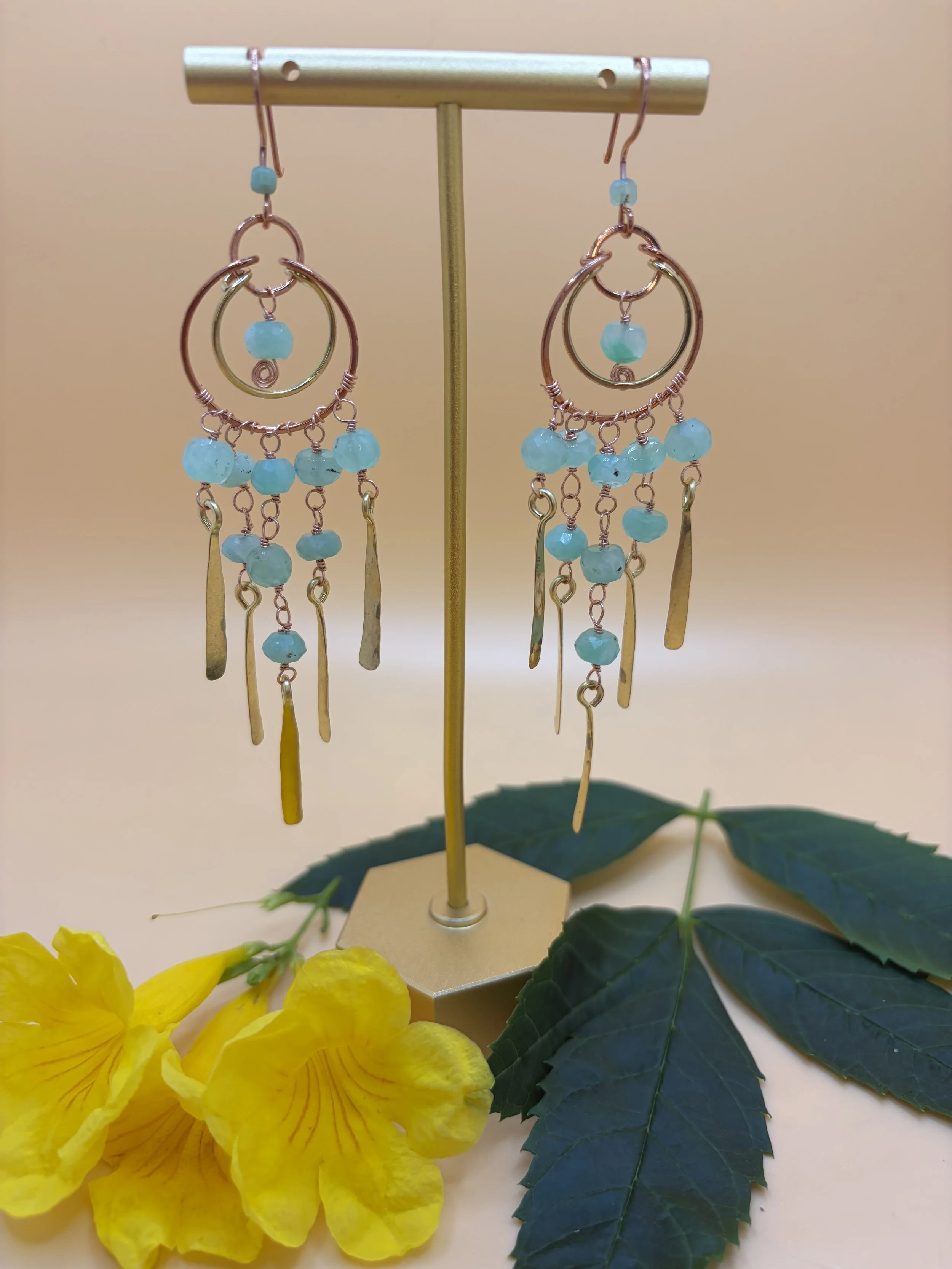Handmade mixed metal chandelier earring worn on an ear, with nested copper and brass hoops, strands of green faceted chrysoprase beads, and hand-hammered paddles.