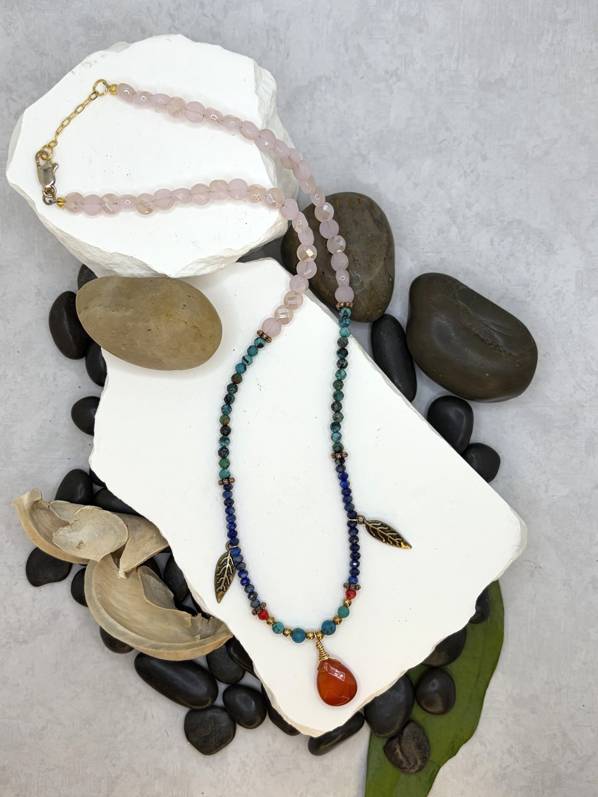 Beaded necklace with carnelian pendant, turquoise, lapis lazuli, pink glass beads, and brass feather charms on a lobster claw clasp.