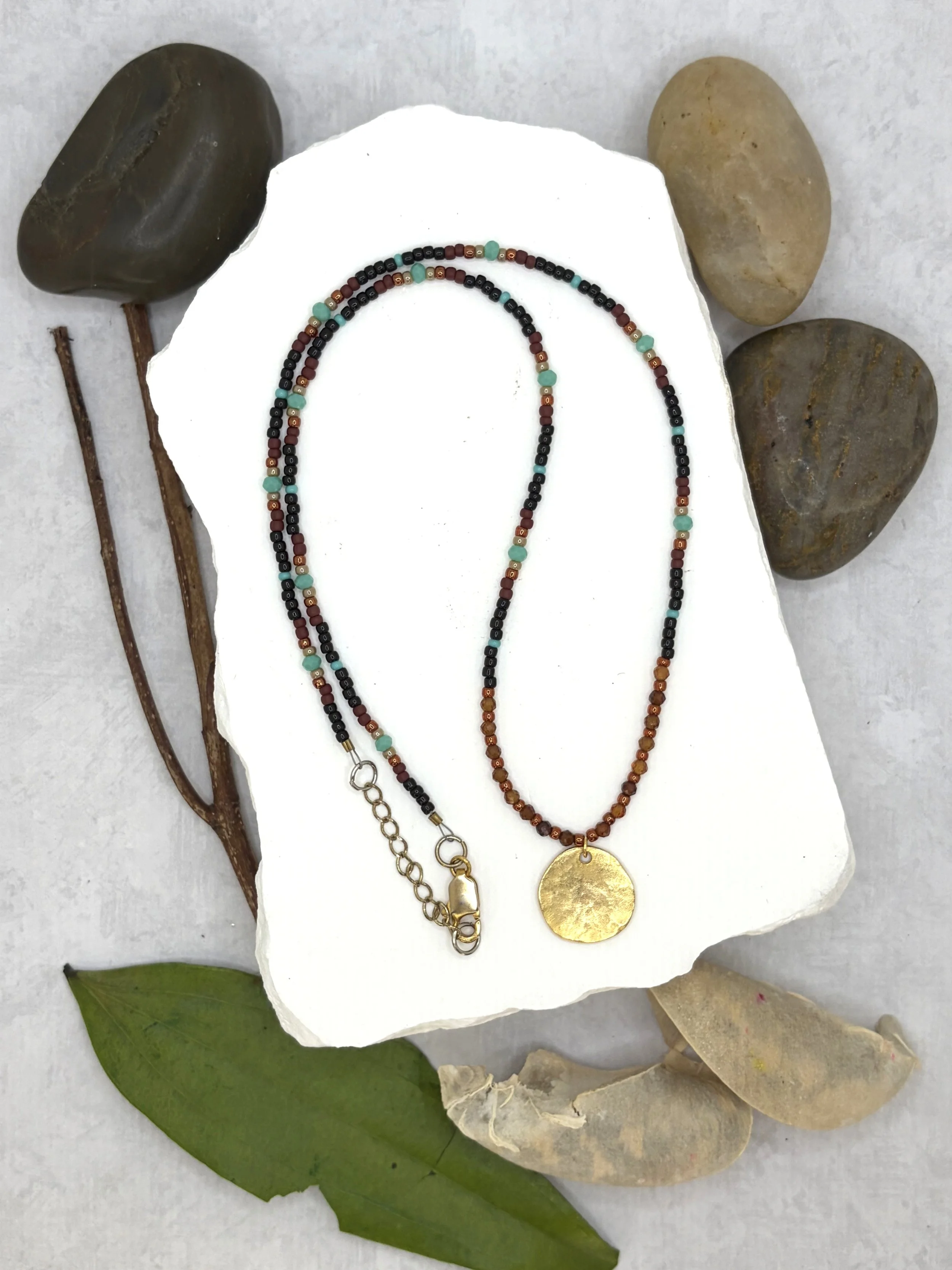Handmade seed bead necklace with faceted garnet beads and a hammered gold-toned disc pendant
