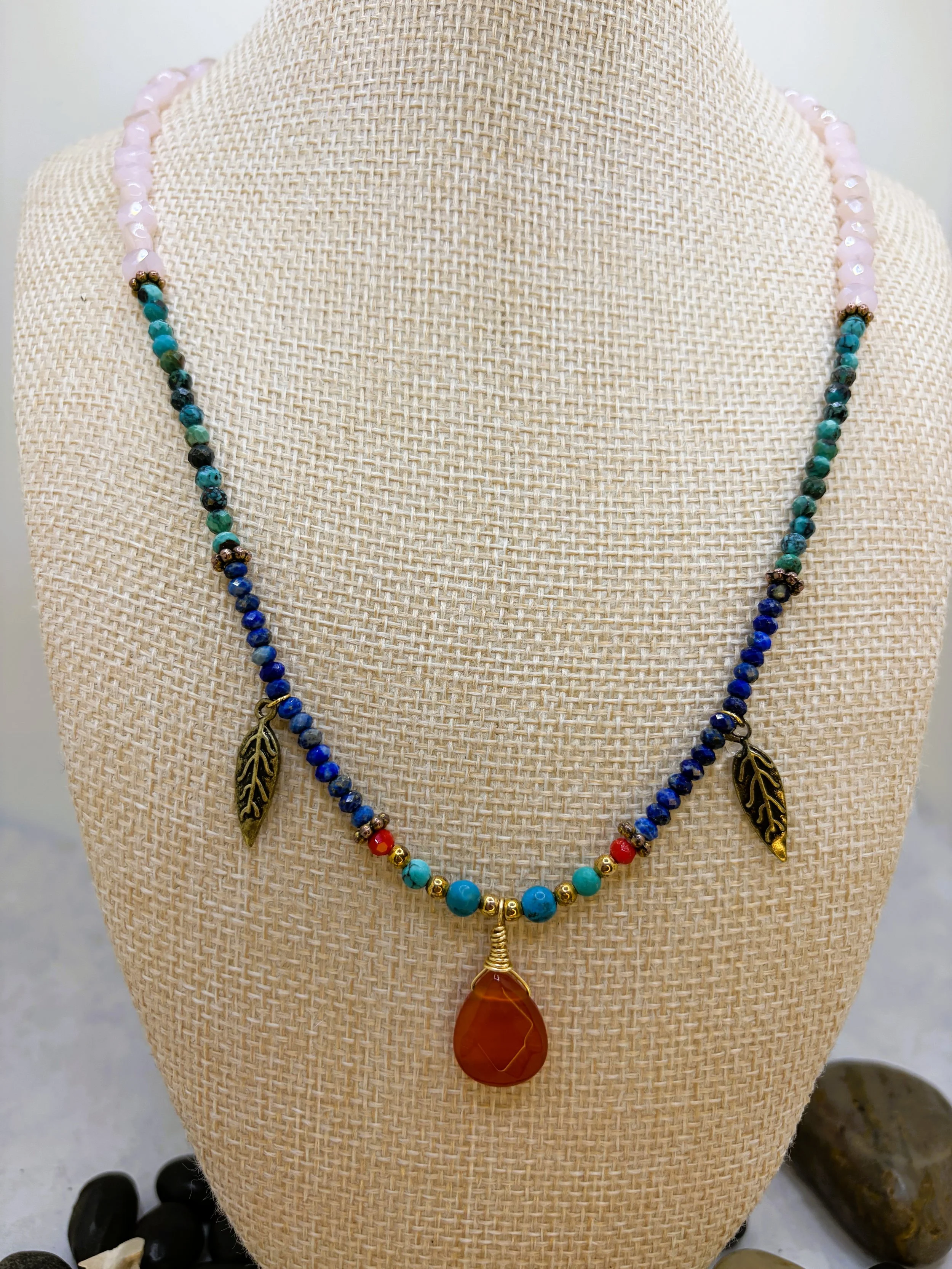 Beaded necklace with carnelian pendant, turquoise, lapis lazuli, pink glass beads, and brass feather charms on a lobster claw clasp.