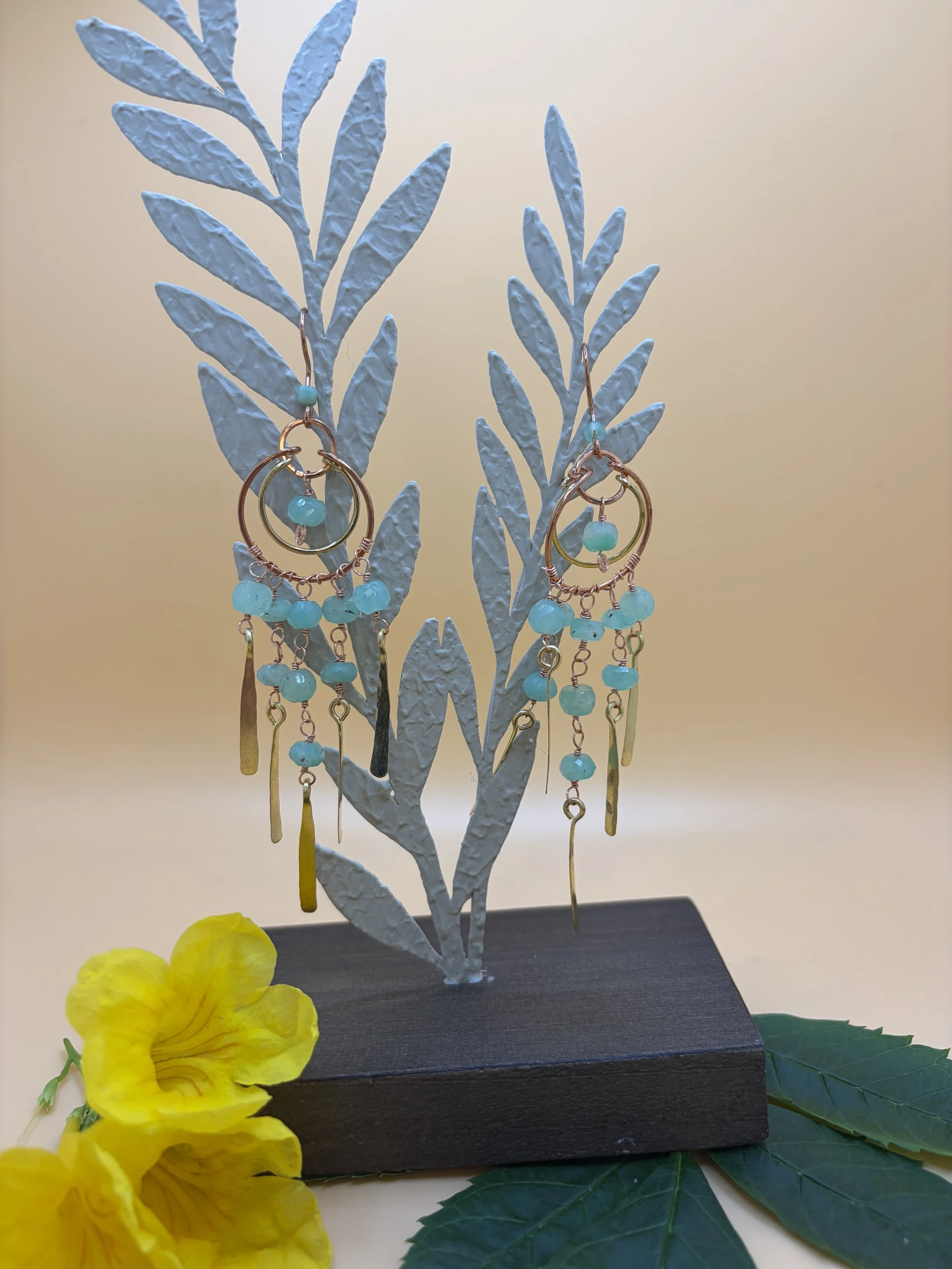 Handmade mixed metal chandelier earring worn on an ear, with nested copper and brass hoops, strands of green faceted chrysoprase beads, and hand-hammered paddles.