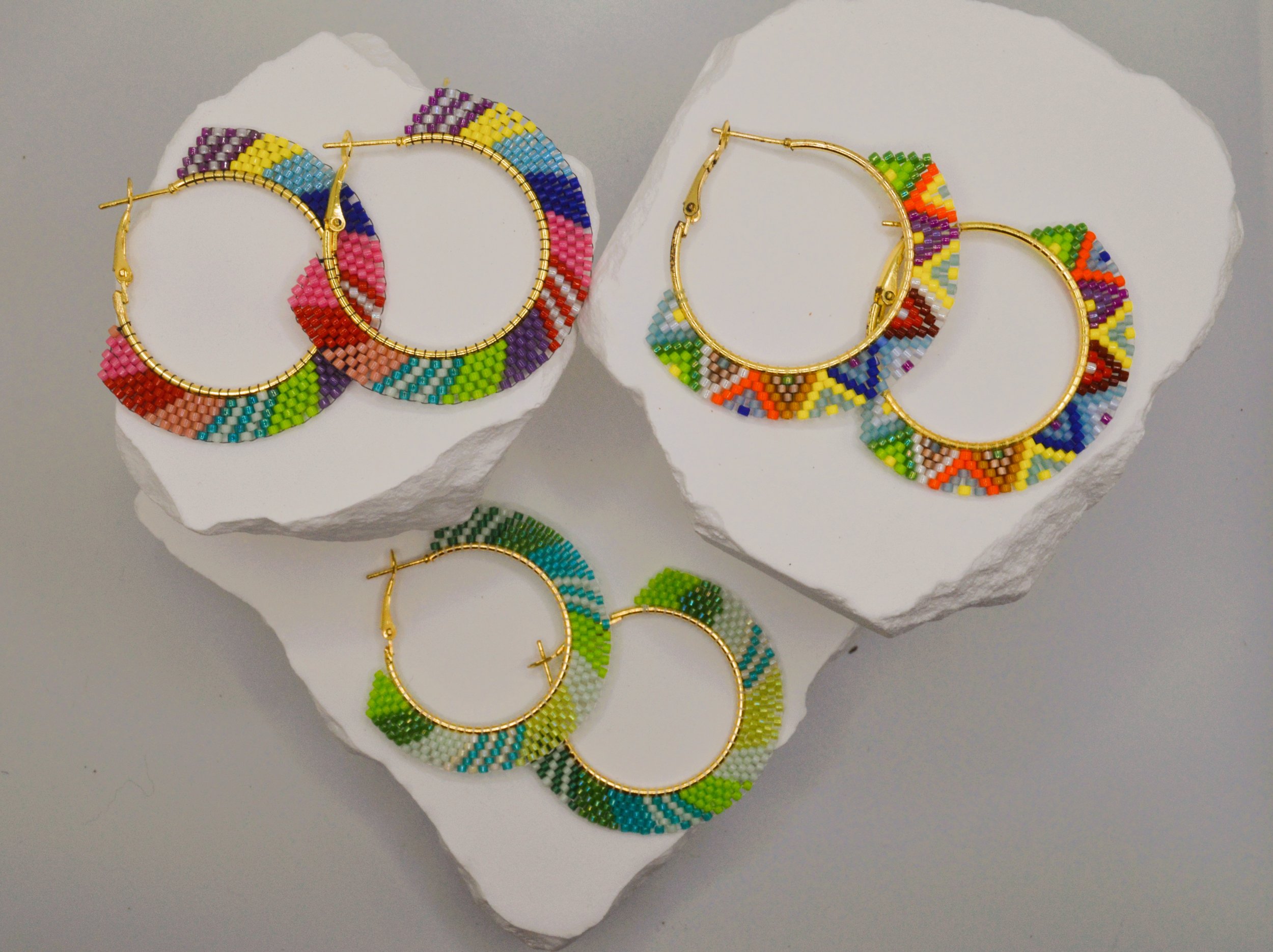 Colorful beaded hoop earrings with a spiral design, displayed on white rocks.
