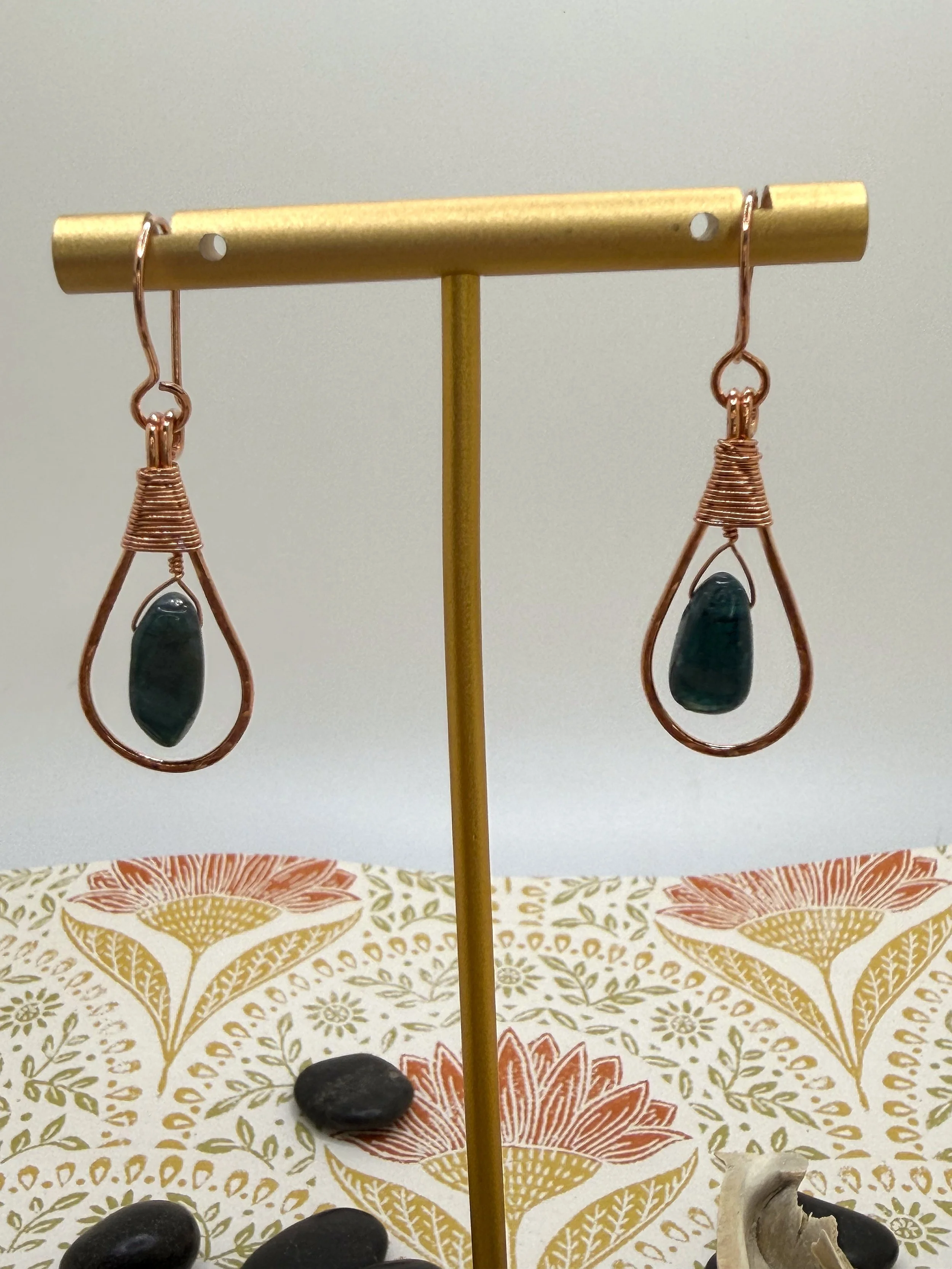 Pair of handmade hammered copper teardrop earrings with coiled wire caps and deep blue tourmaline beads on a wooden slice