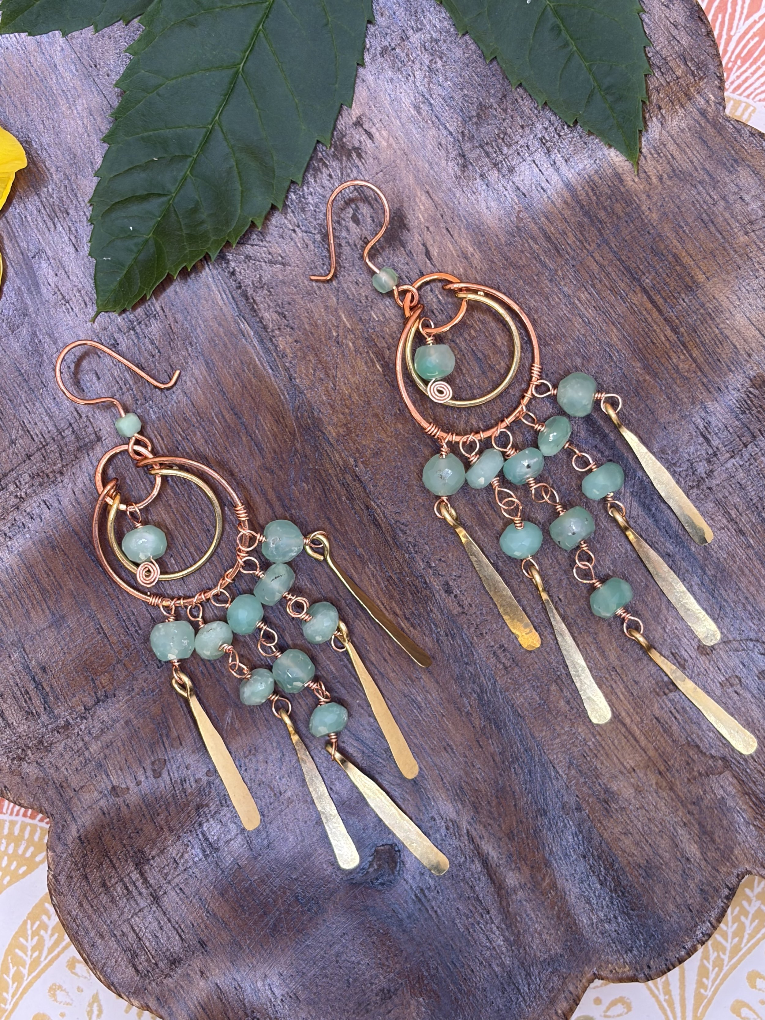 Handmade mixed metal chandelier earring worn on an ear, with nested copper and brass hoops, strands of green faceted chrysoprase beads, and hand-hammered paddles.