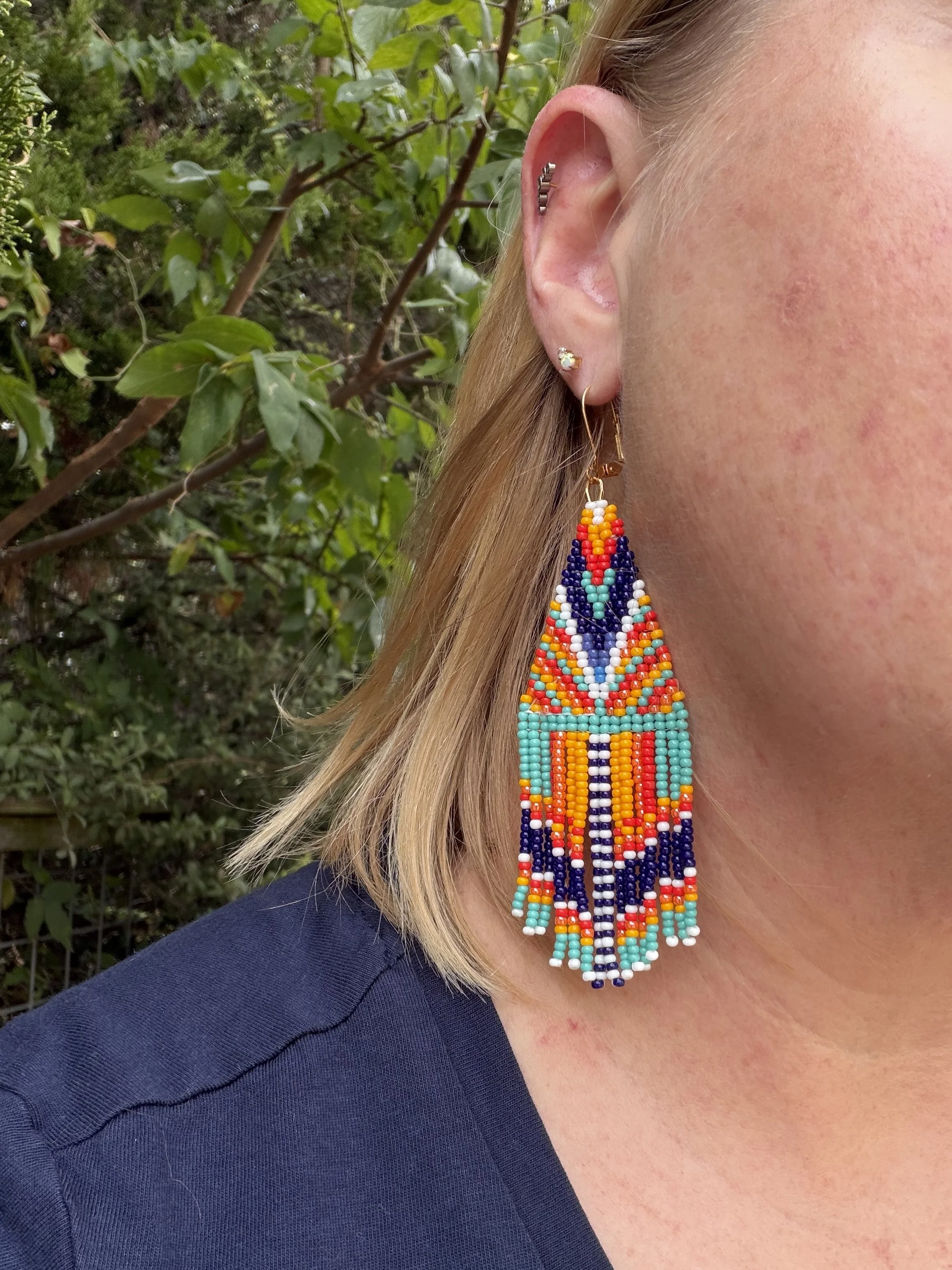 Woman wearing handmade geometric seed bead fringe earrings, turquoise coral marigold navy and white, gold ear wire