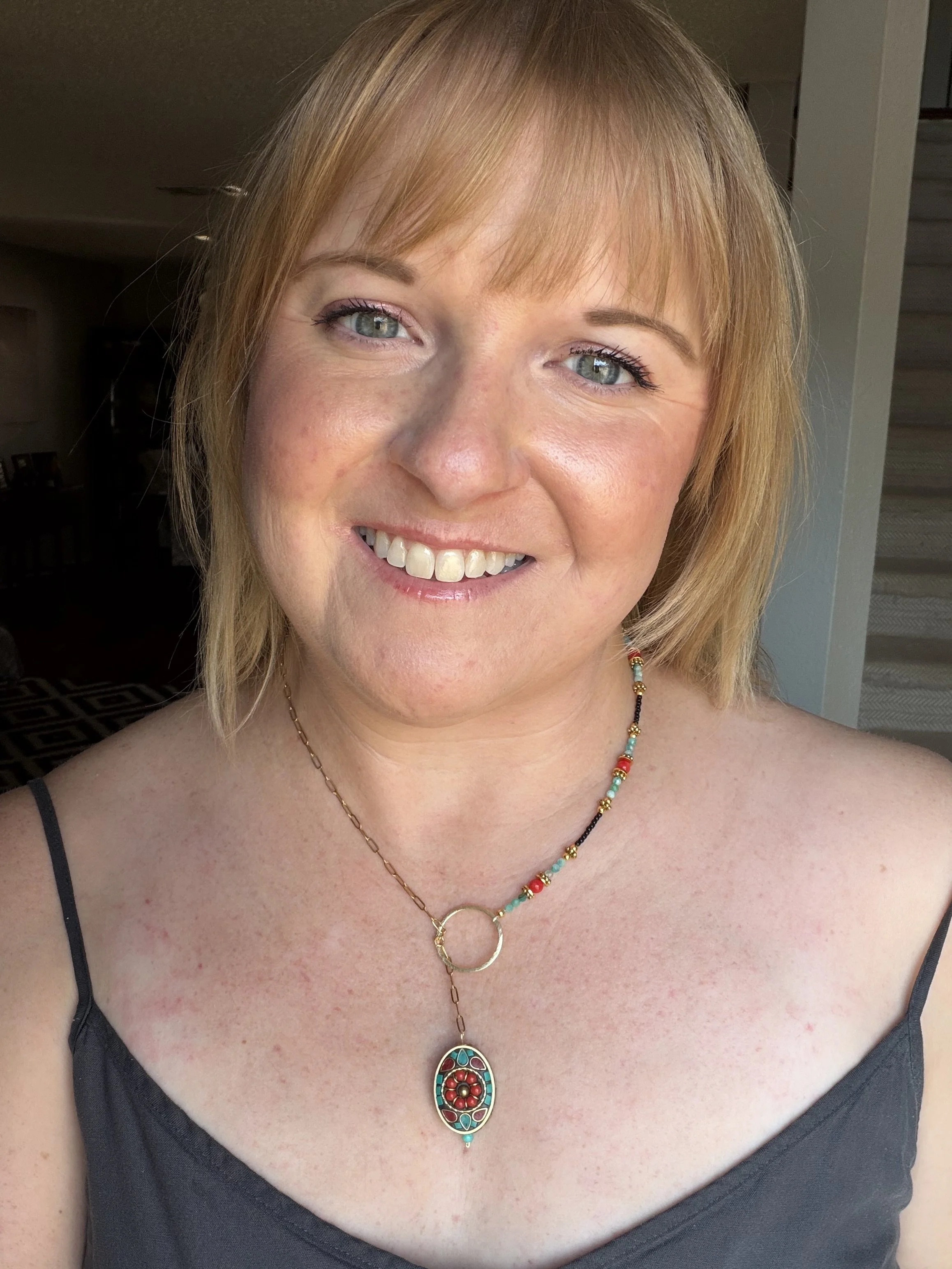 woman wearing Handmade asymmetrical necklace with a Tibetan brass coral and turquoise howlite inlay pendant, red coral and amazonite beads, and a gold-toned paperclip chain