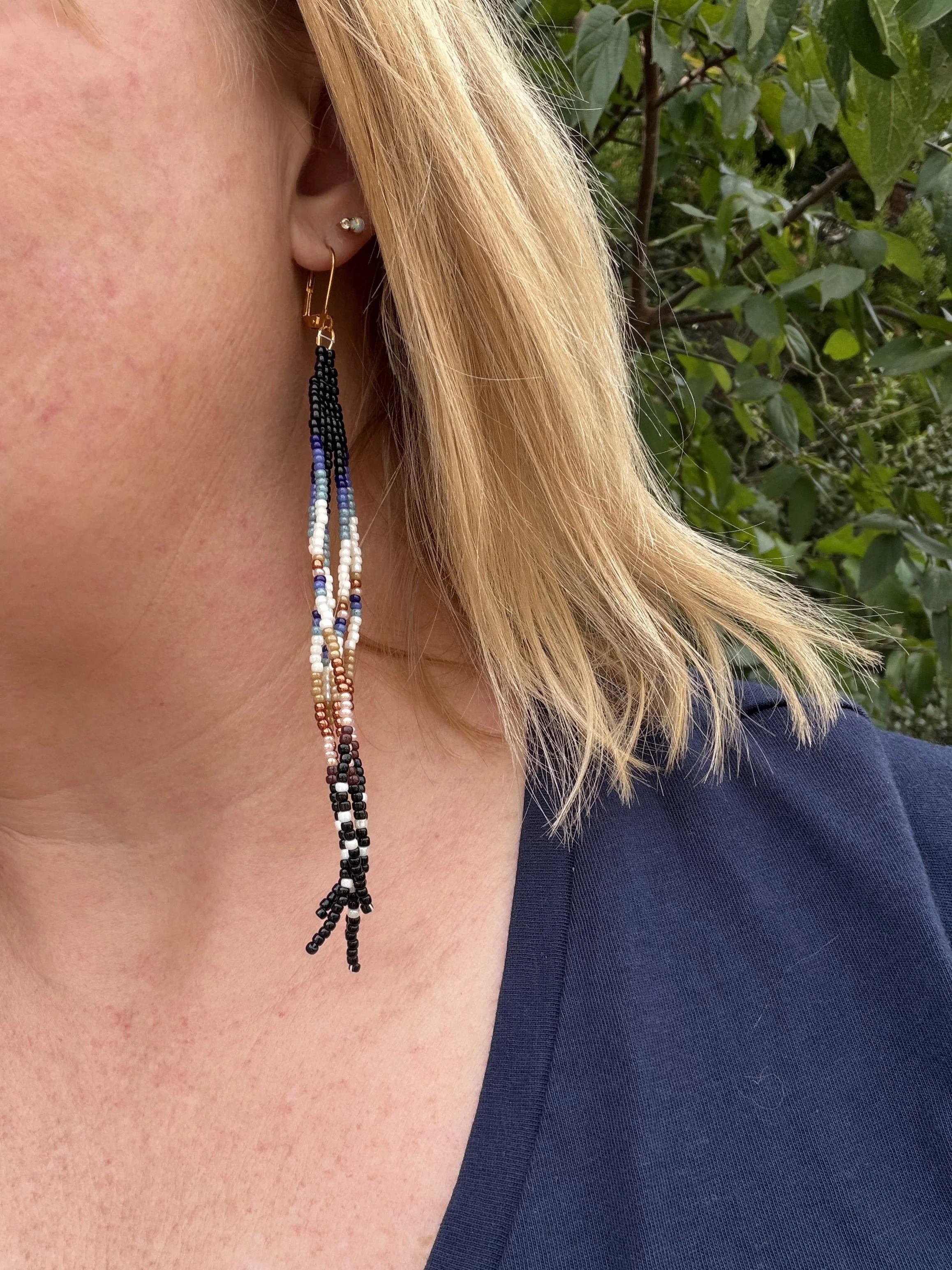 closeup of handmade seed bead fringe earrings, black navy teal cream tan terracotta and blush ombre, gold ear wire