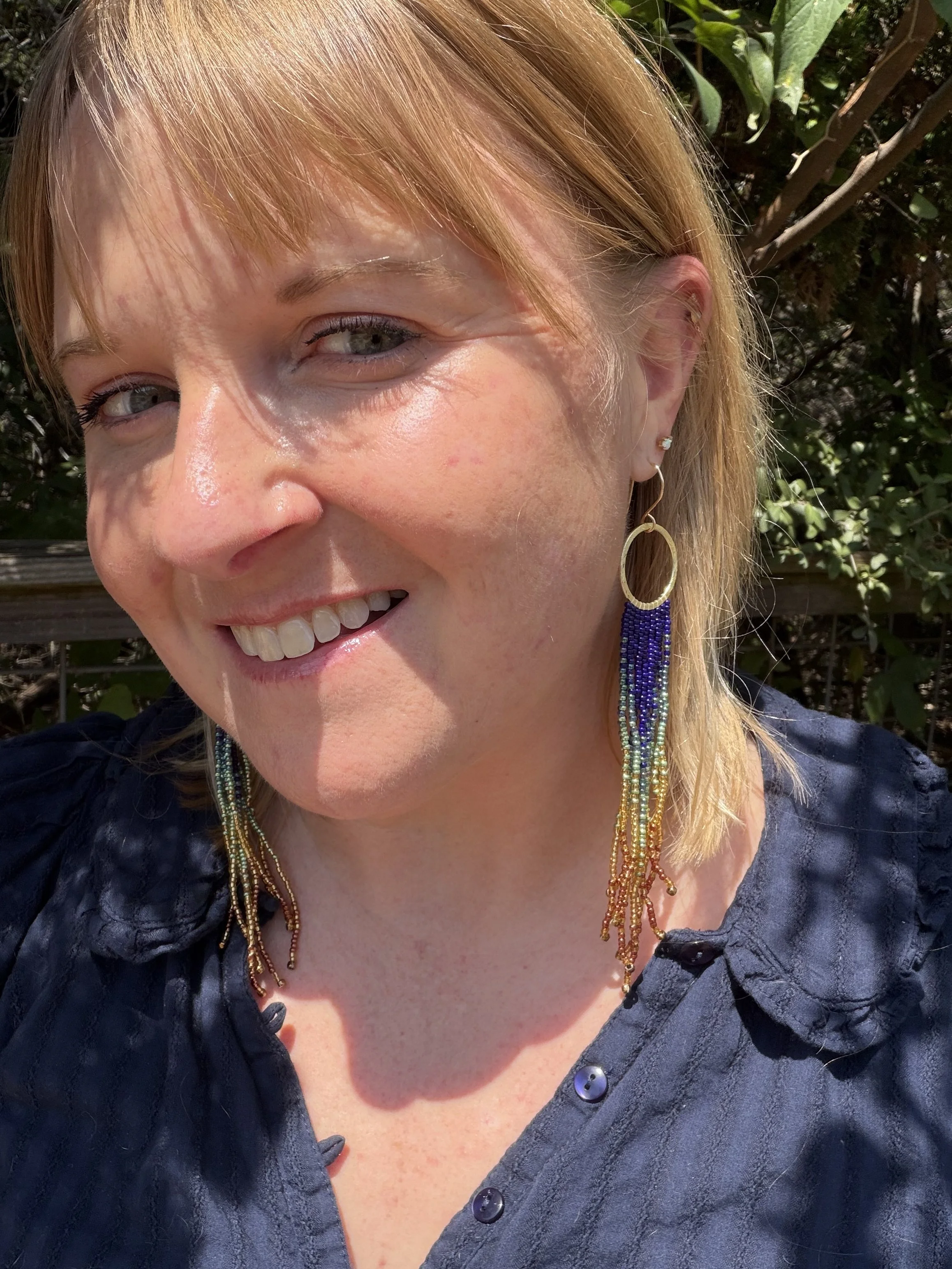 woman wearing handmade seed bead fringe earrings on gold hoops, navy teal gold and copper ombre, gold-filled ear wire