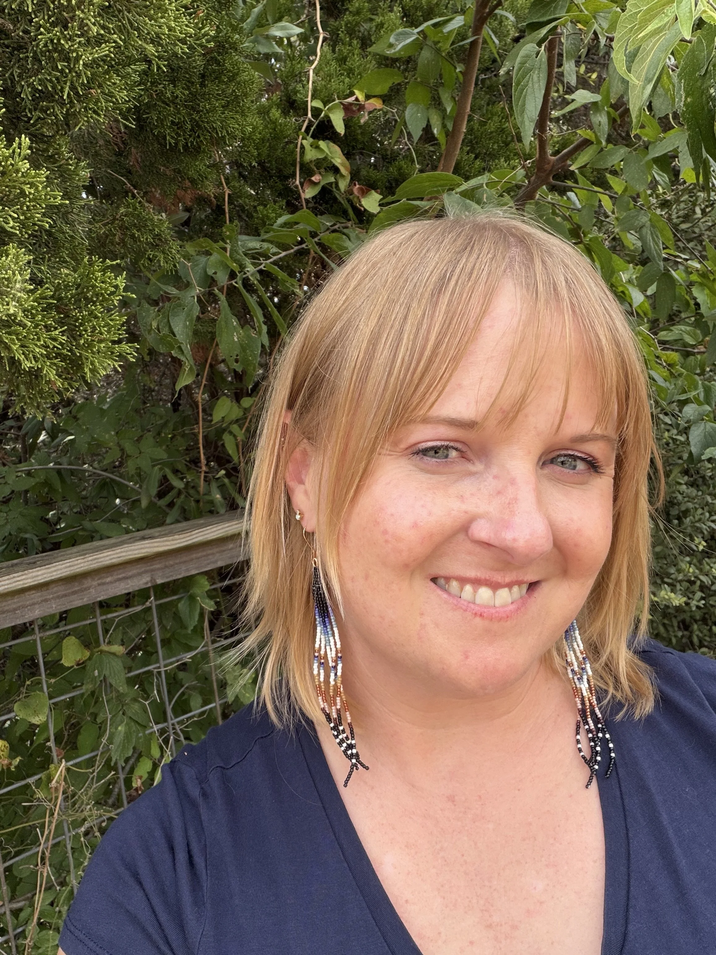 Woman wearing handmade seed bead fringe earrings, black navy teal cream tan terracotta and blush ombre, gold ear wire