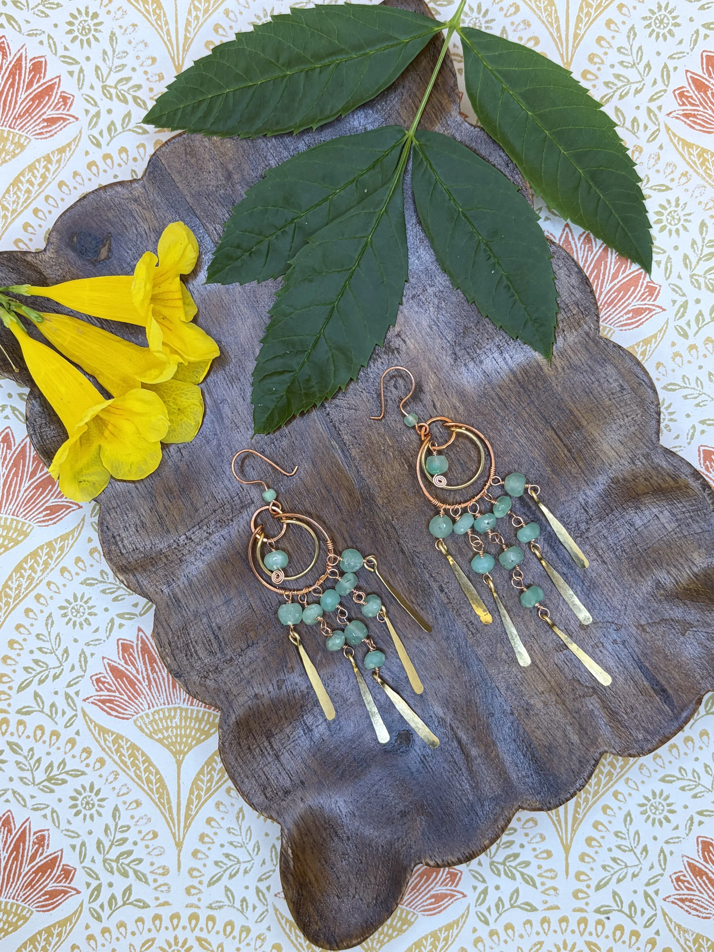 Handmade mixed metal chandelier earring worn on an ear, with nested copper and brass hoops, strands of green faceted chrysoprase beads, and hand-hammered paddles.