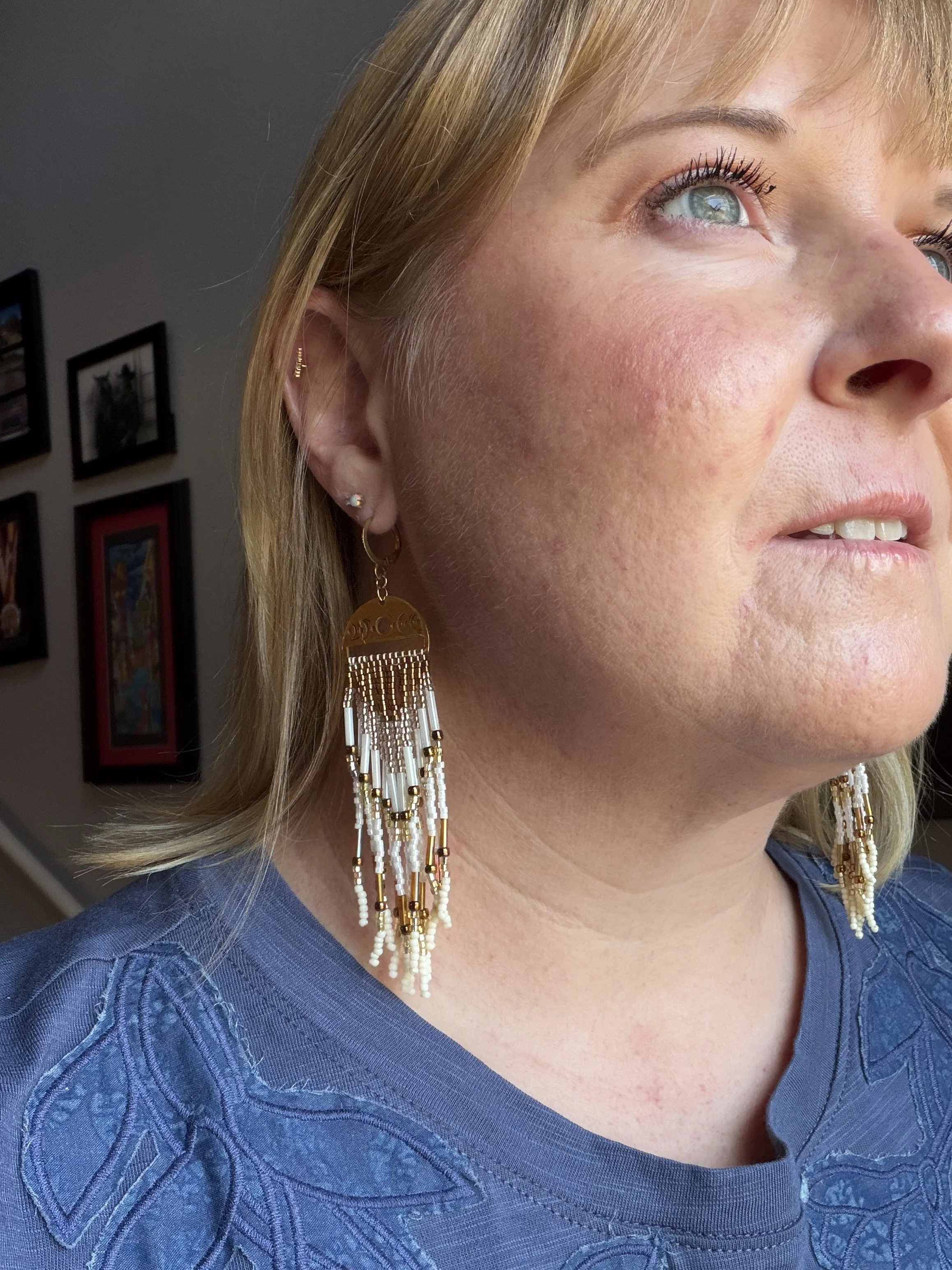 woman wearing handmade seed bead fringe earrings with brass moon phase charm and cream bronze gold beading