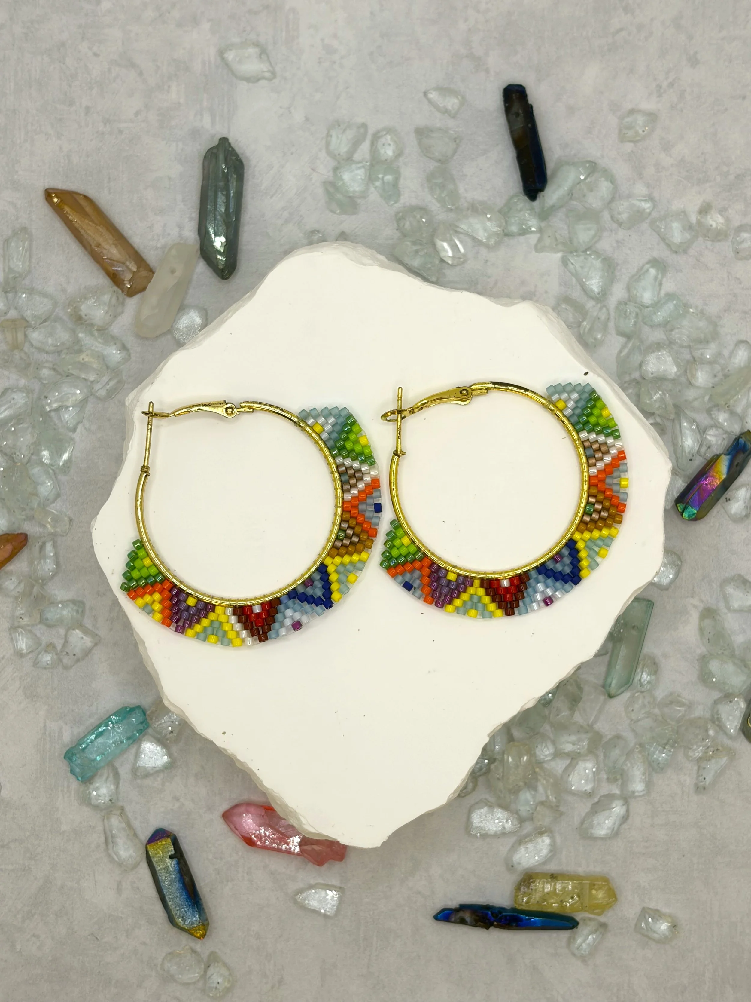 Multicolor seed bead woven hoop earrings in gold-tone metal with a geometric rainbow pattern.