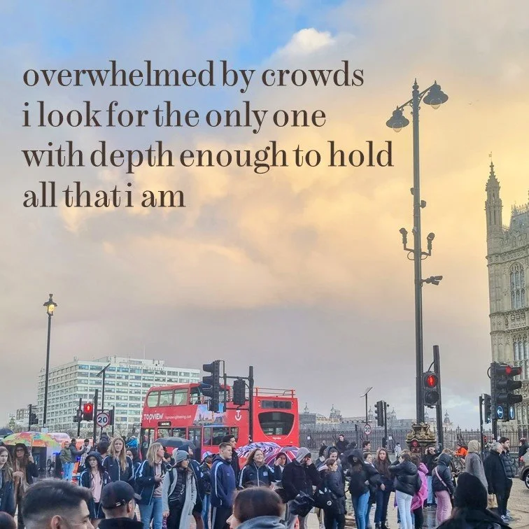 Crowds of people gathered on a street in London with the Houses of Parliament and Big Ben visible in the background, under a sky with clouds and a setting sun.