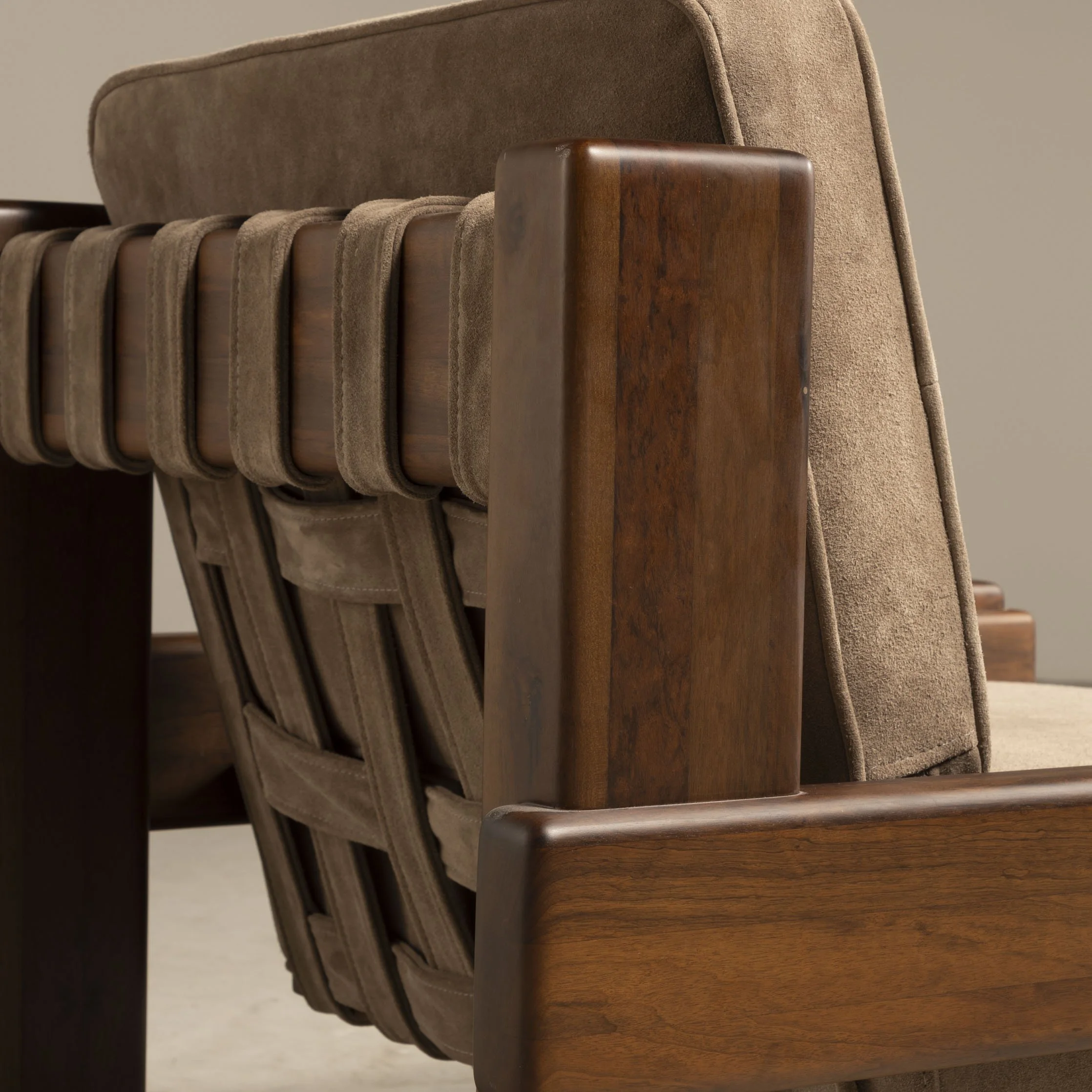 Detalhes de uma poltrona de madeira com estofado bege, foco na lateral do braço e no encosto.