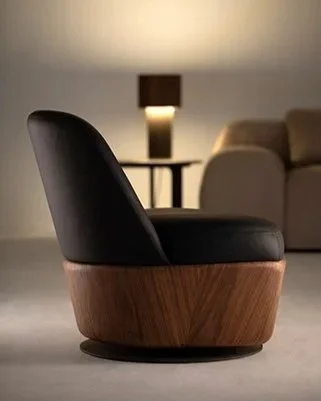 Poltrona moderna de madeira e couro escuro em um ambiente de sala, com luminária ao fundo.