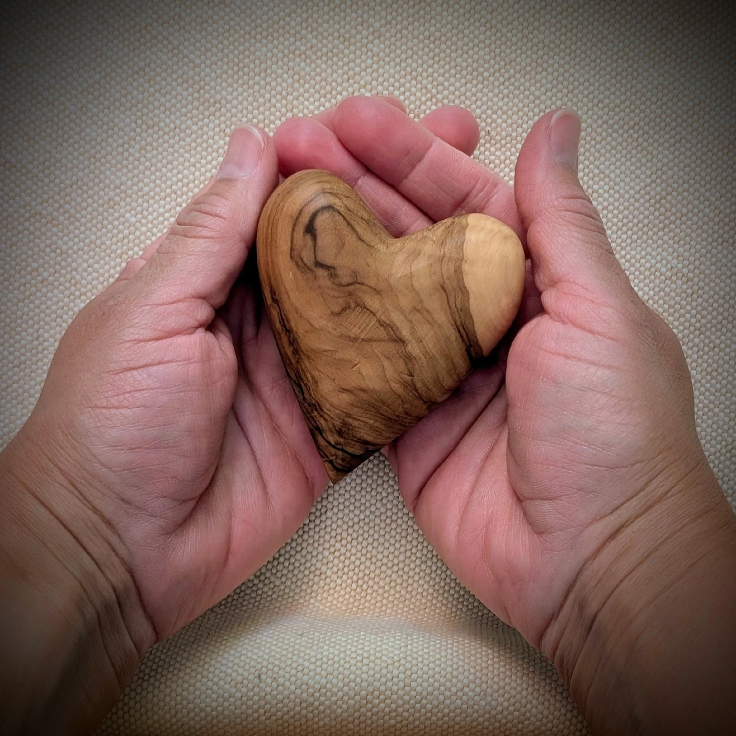 Two hands gently holding a small wooden heart