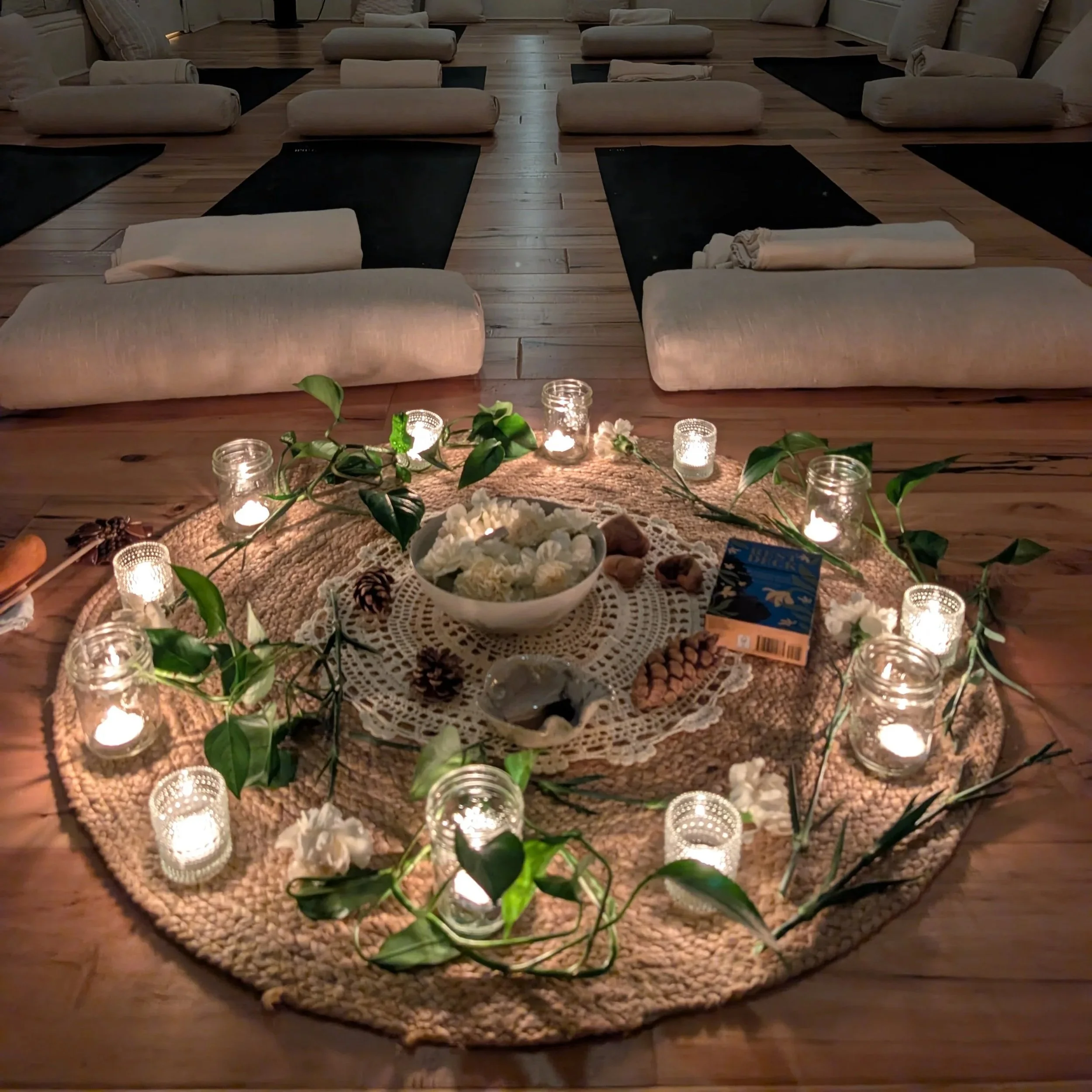 Mats, bolsters, blankets, and candles arranged around a central display for a collective rest gathering