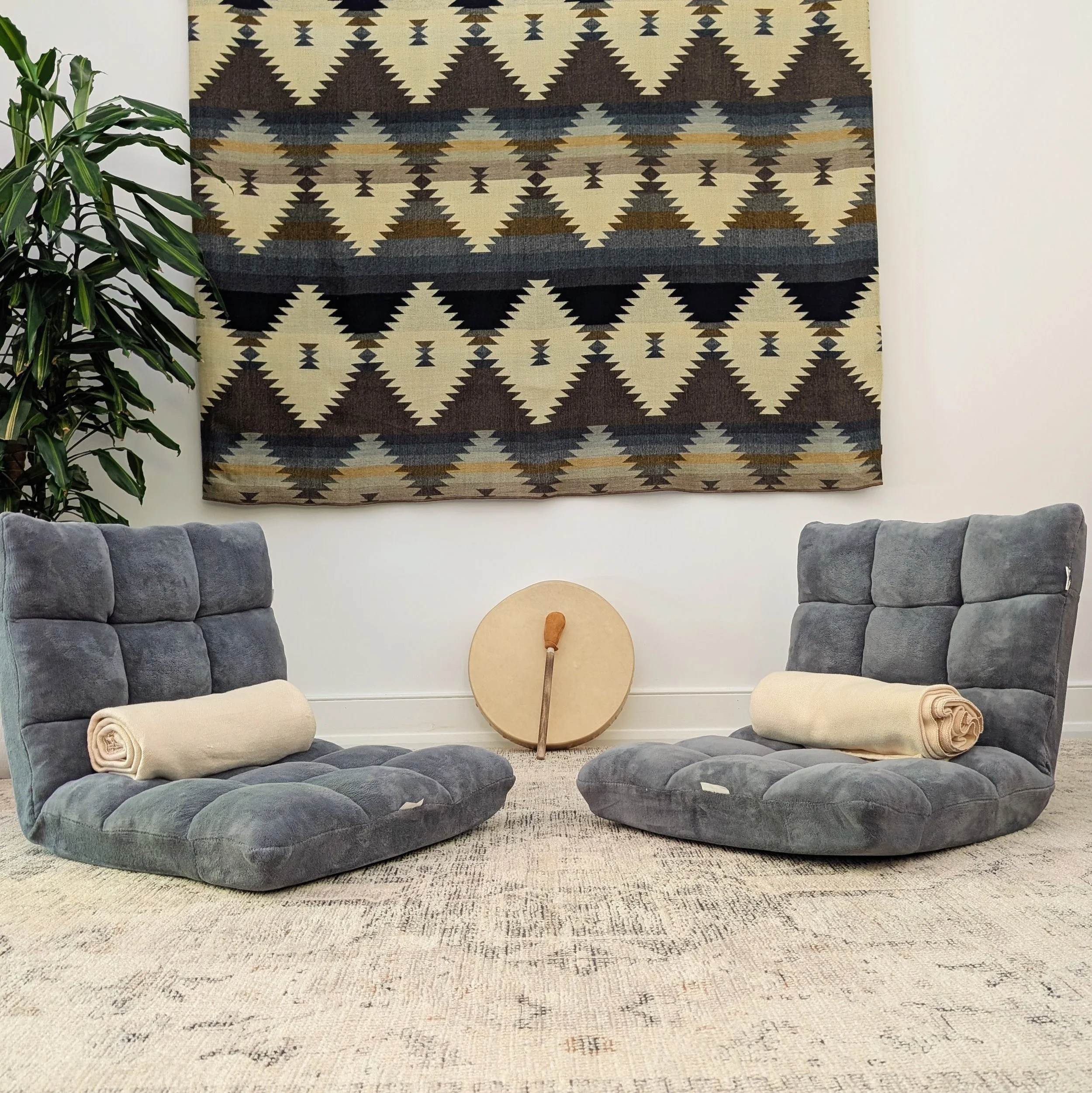 Two cushioned floor chairs with blankets and a frame drum in a quiet somatic coaching space