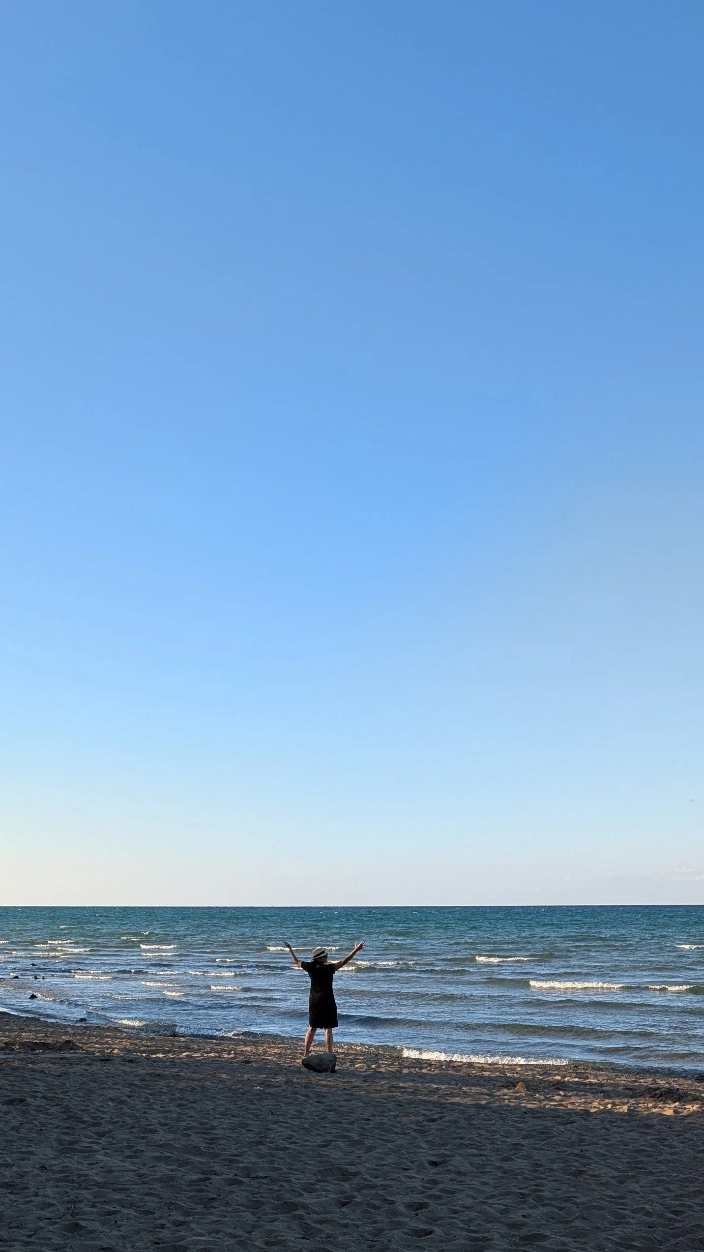Woman with outstretched arms in front of open water and blue sky