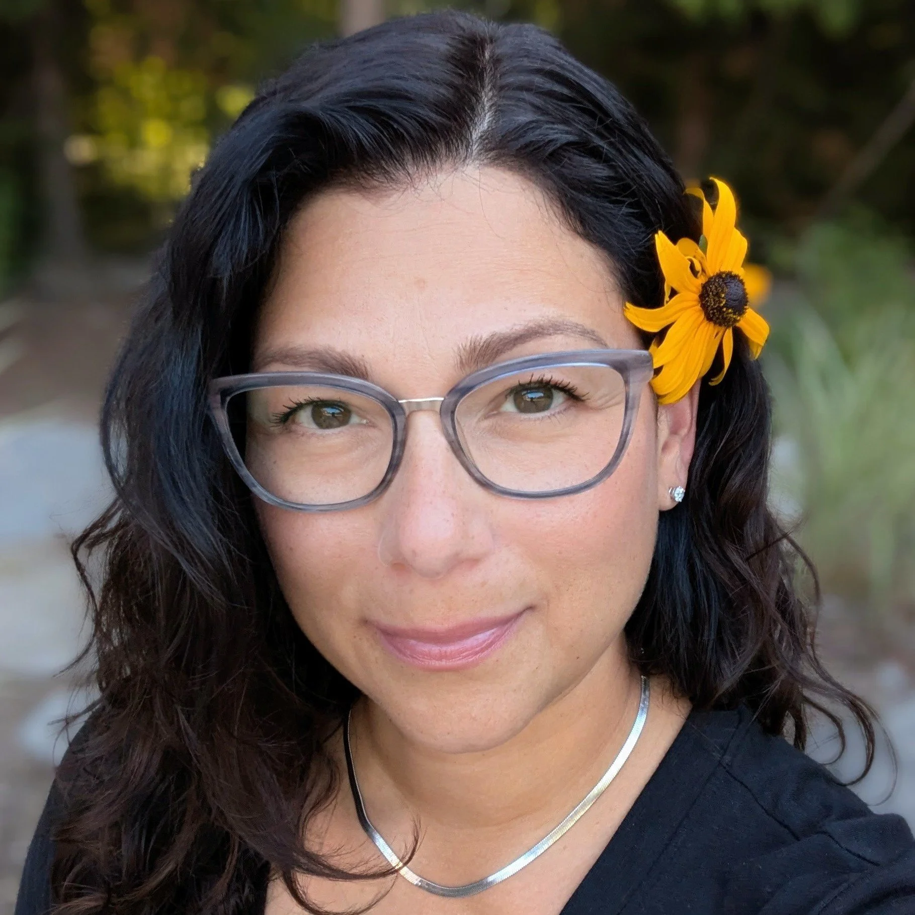 Disa Almeida smiling outdoors with a yellow flower in her hair