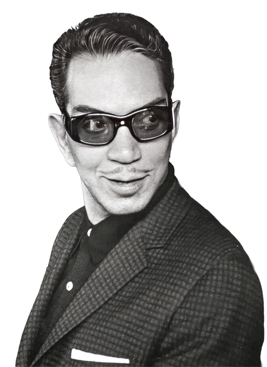 Retrato en blanco y negro de Mario Moreno Reyes con gafas oscuras, cabello peinado hacia atrás, vestimenta formal con saco y camisa, sonriendo ligeramente, estilo vintage de los años 50
