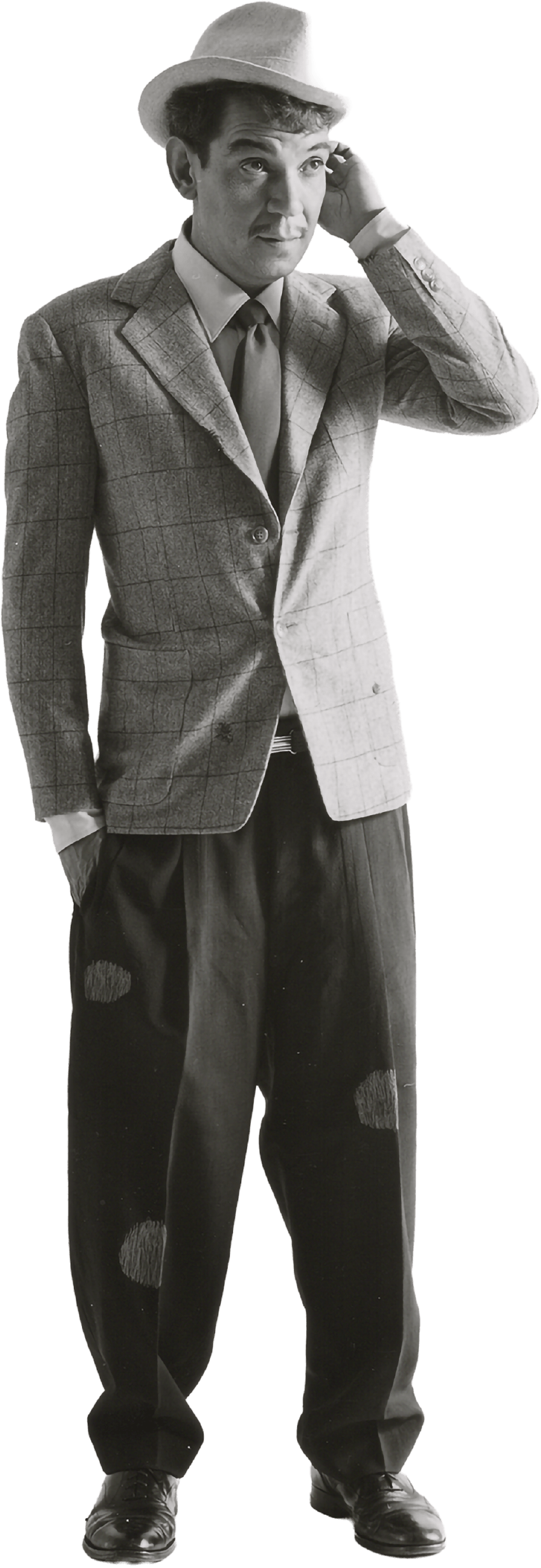 Cantinflas con sombrero, saco a cuadros, camisa blanca, corbata y pantalones anchos con parches, ajustados con zapatos formales. Tocándose la cabeza con la mano izquierda.