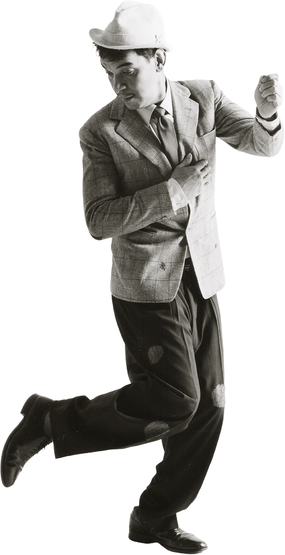 Cantinflas con sombrero, saco a cuadros, camisa blanca, corbata y pantalones anchos con parches, ajustados con zapatos formales. Practicando un paso de baile, volteando hacia abajo para ver su zapato.