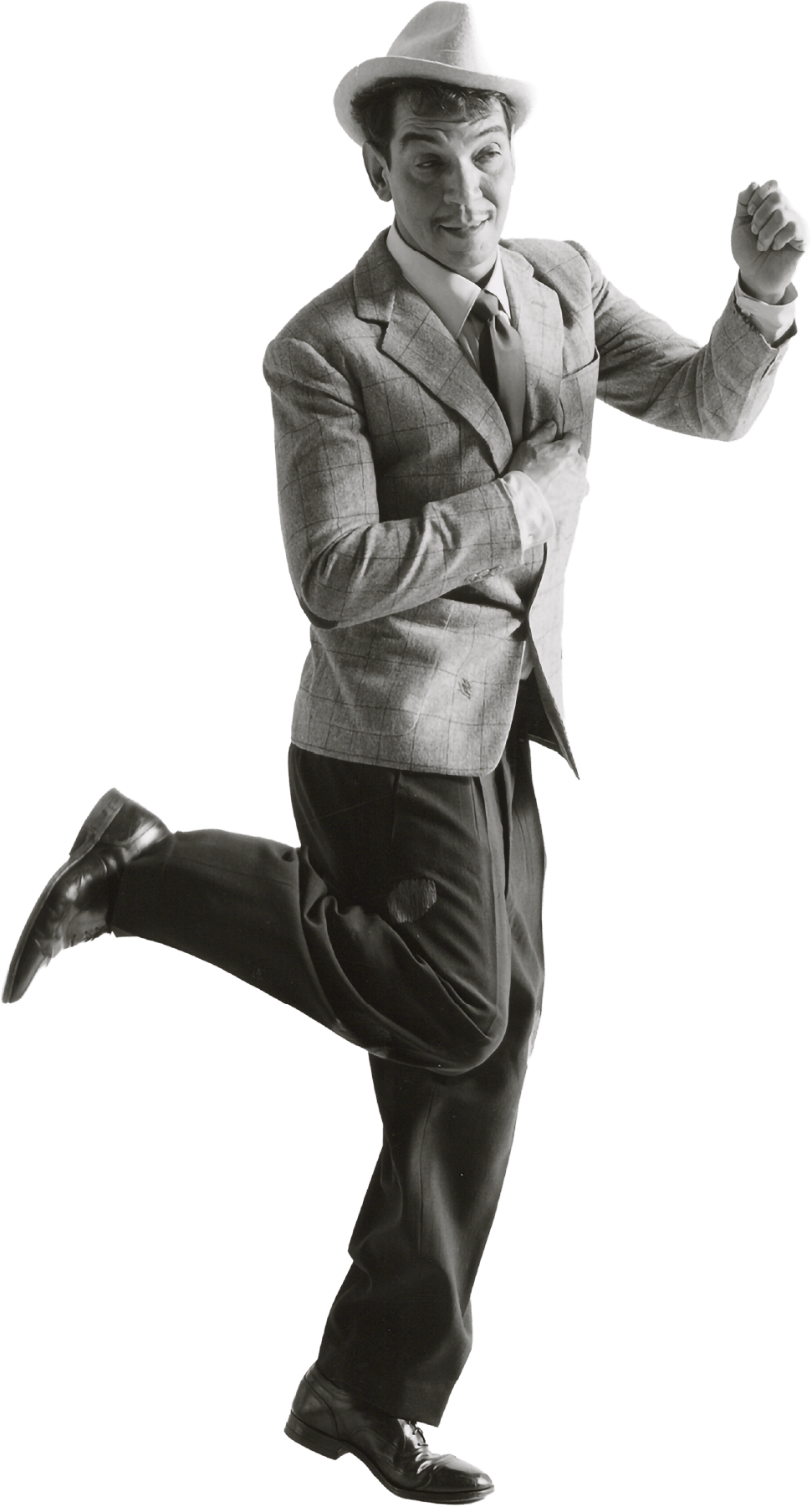 Cantinflas con sombrero, saco a cuadros, camisa blanca, corbata y pantalones anchos con parches, ajustados con zapatos formales. Practicando un paso de baile y con los ojos medio cerrados.