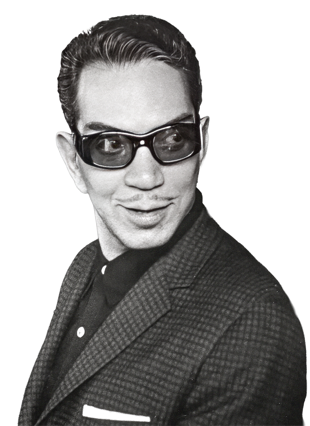 Retrato en blanco y negro de Mario Moreno Reyes con gafas oscuras, cabello peinado hacia atrás y saco a cuadros, sonriendo ligeramente y mirando hacia la derecha.