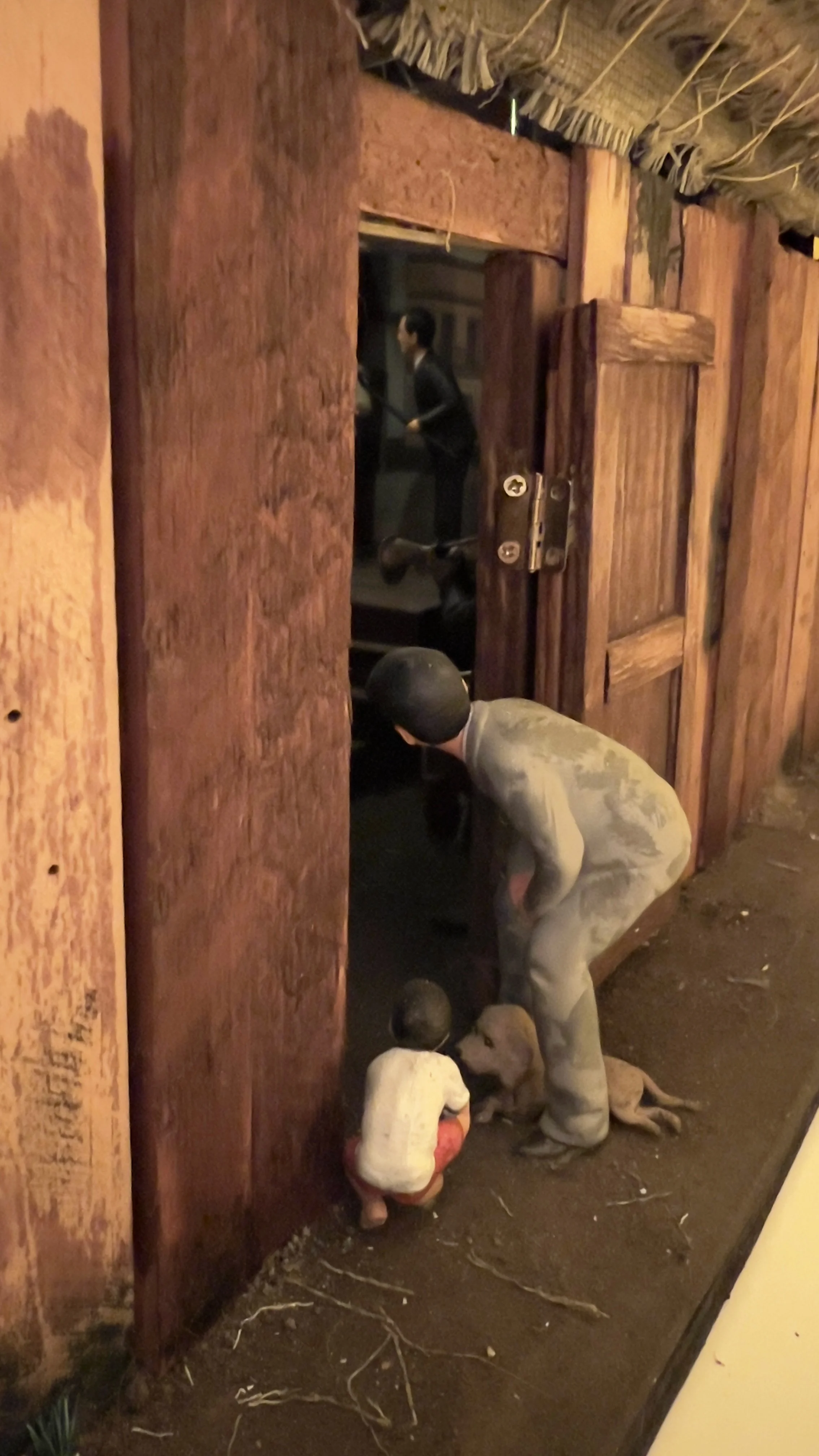 Dos niños y un adulto se asoman al interior de la Carpa Valentina, en una recreación nocturna con estructuras de madera y paja.