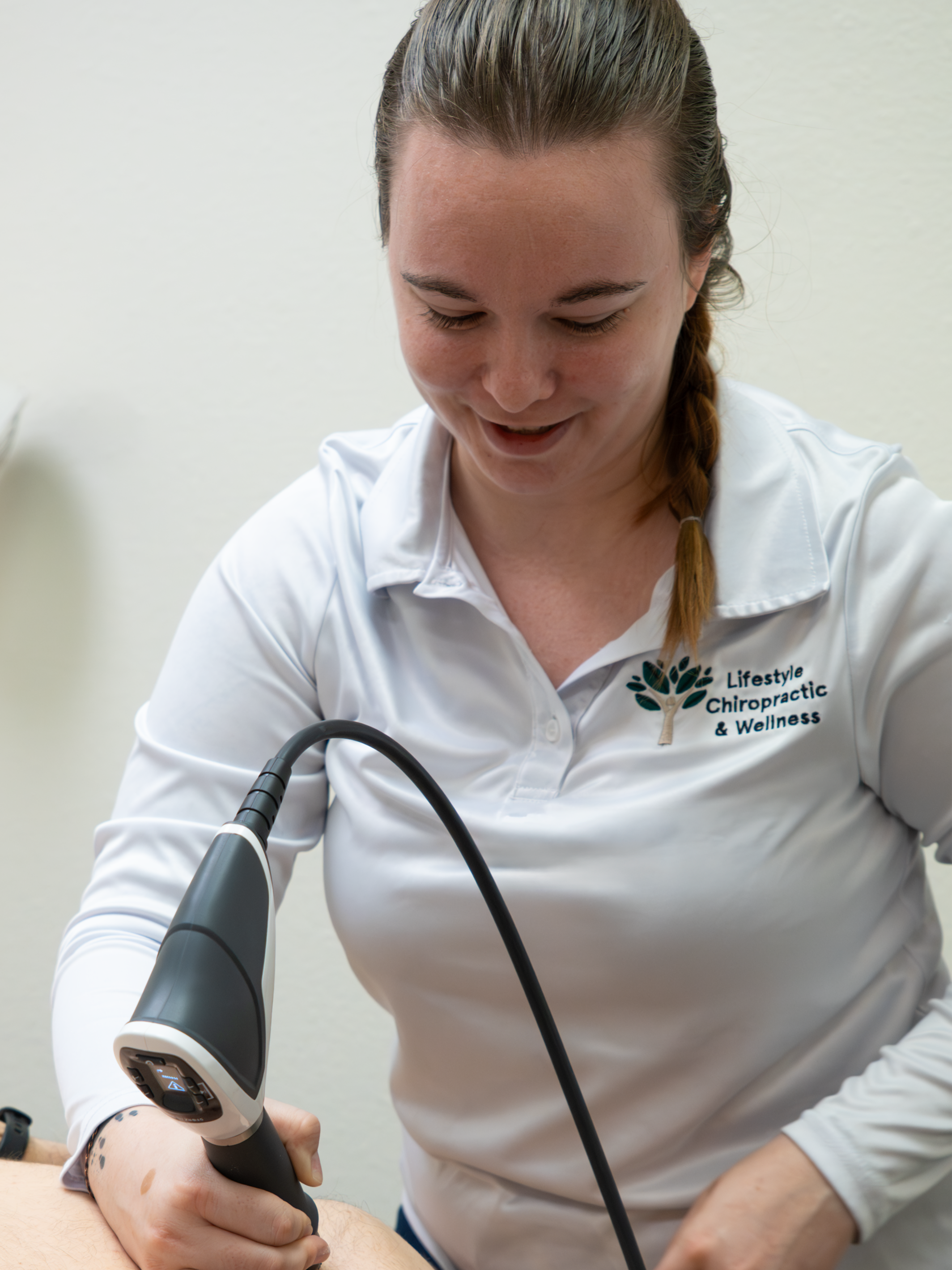 Chiropractor performing a shock wave therapy treatment on a patient's back in a clinical setting.