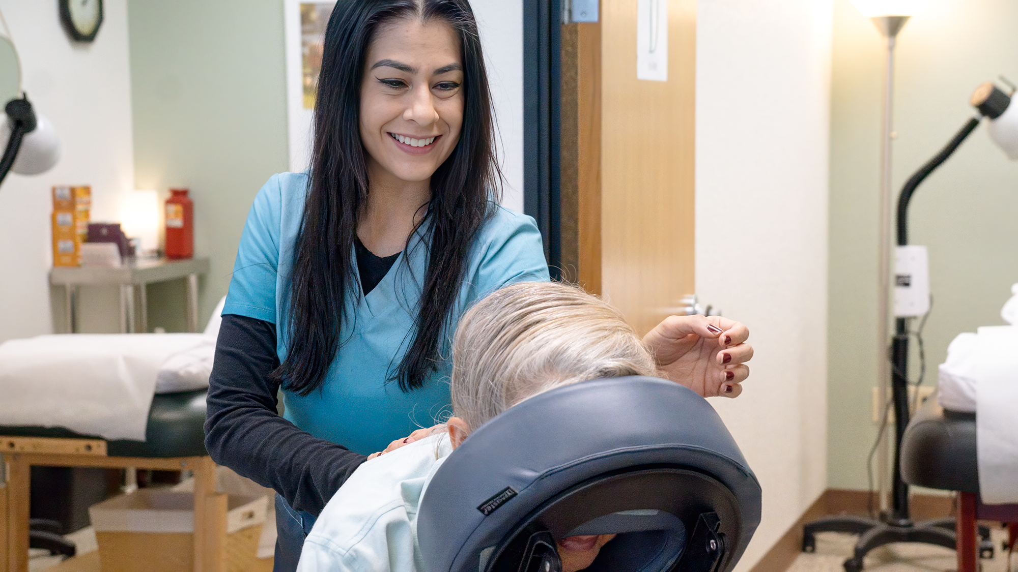 A healthcare worker smiling as they care for an elderly patient in a medical setting.