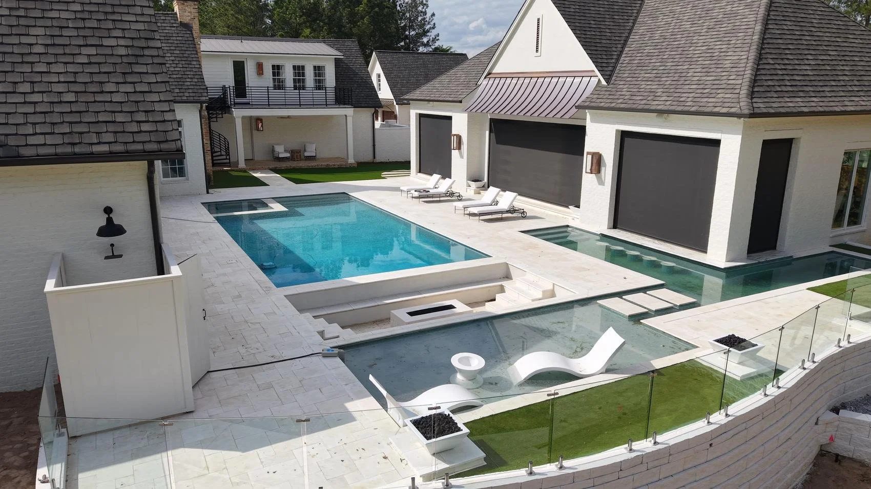 A luxury backyard pool and spa with travertine decking and glass railing installed by SchoggenScapes.jpg