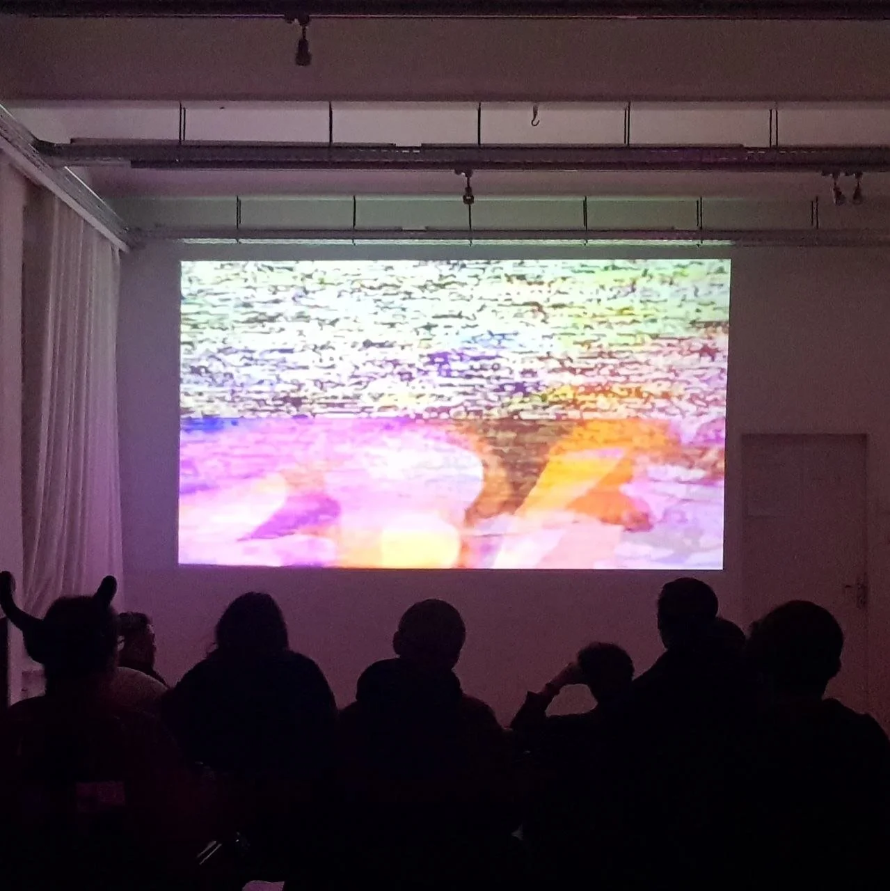 People watching a projection of colorful abstract visuals on a screen in a dark room.