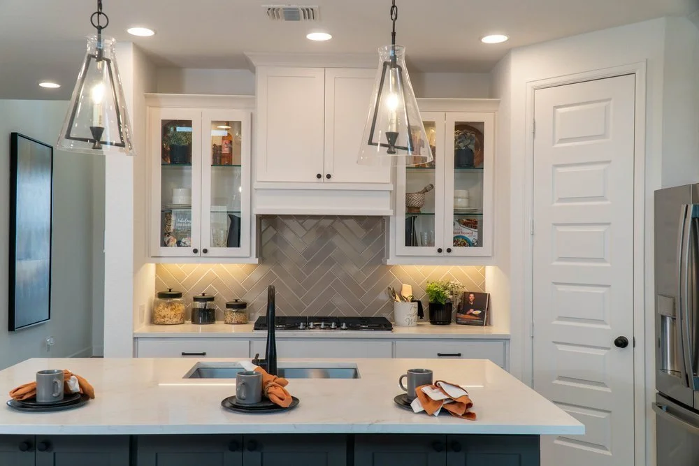 Modern kitchen with white cabinets, gray backsplash, and island with four place settings, two with orange napkins and cups.
