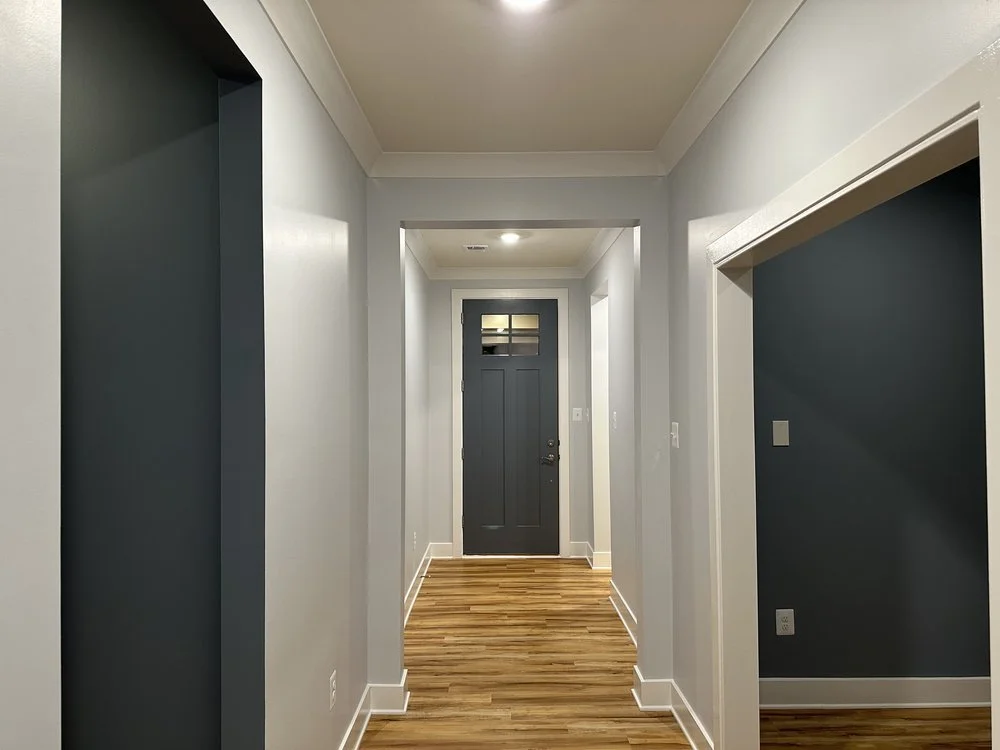 Empty hallway in a house with gray walls, hardwood floors, and a black front door.