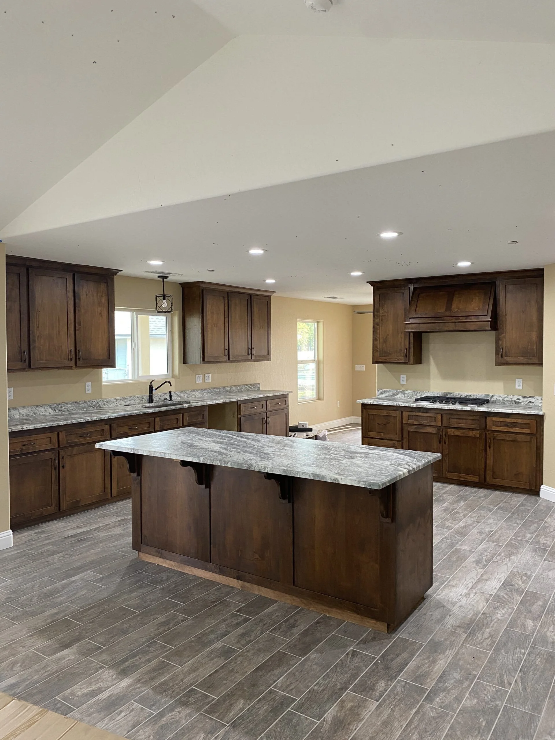 Modern kitchen with dark wooden cabinets, a marble island, and tiled flooring.
