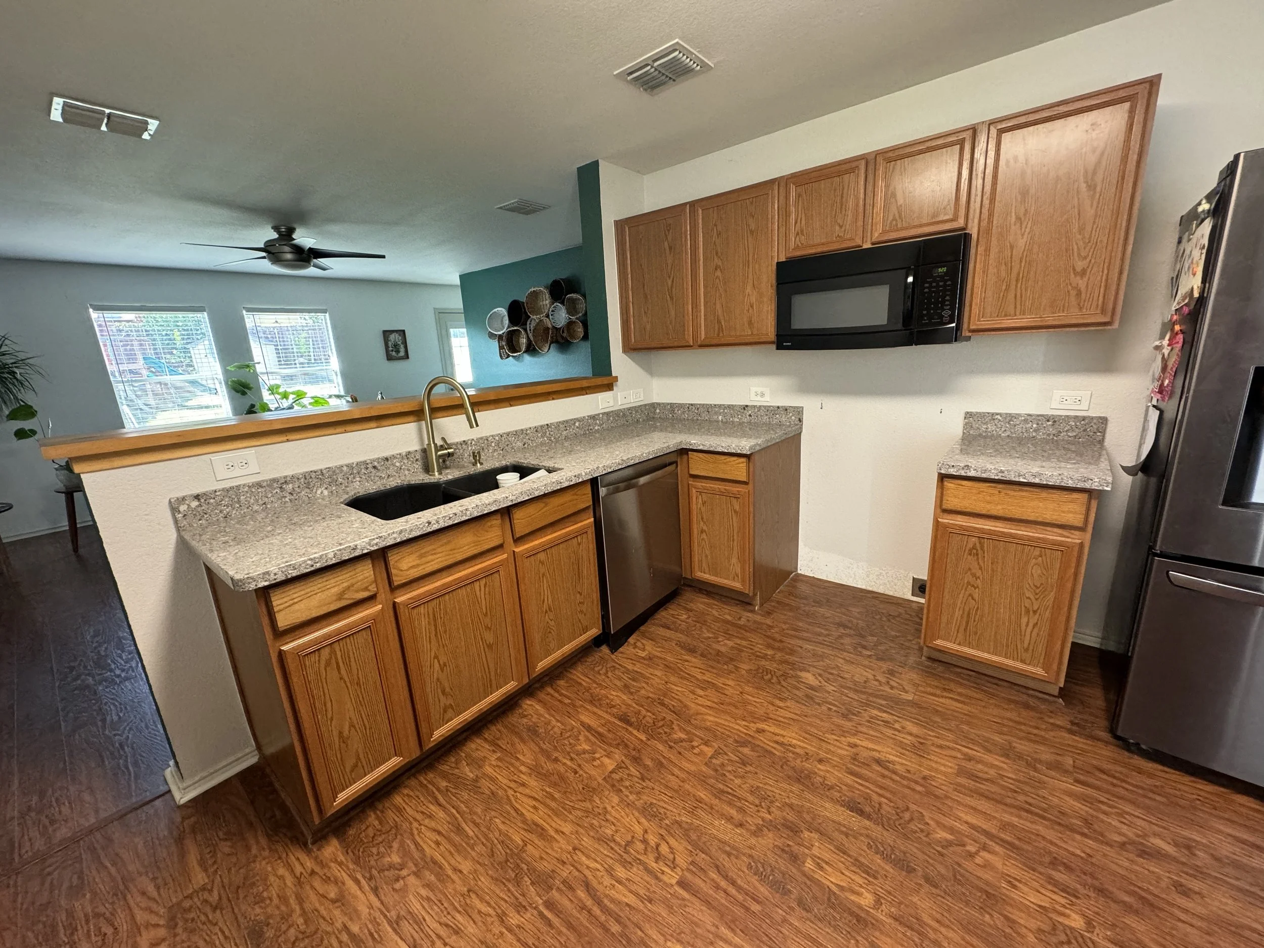Kitchen with wooden cabinets, granite countertops, stainless steel dishwasher and refrigerator, microwave oven, and hardwood floor. A half wall separates the kitchen from the living room.
