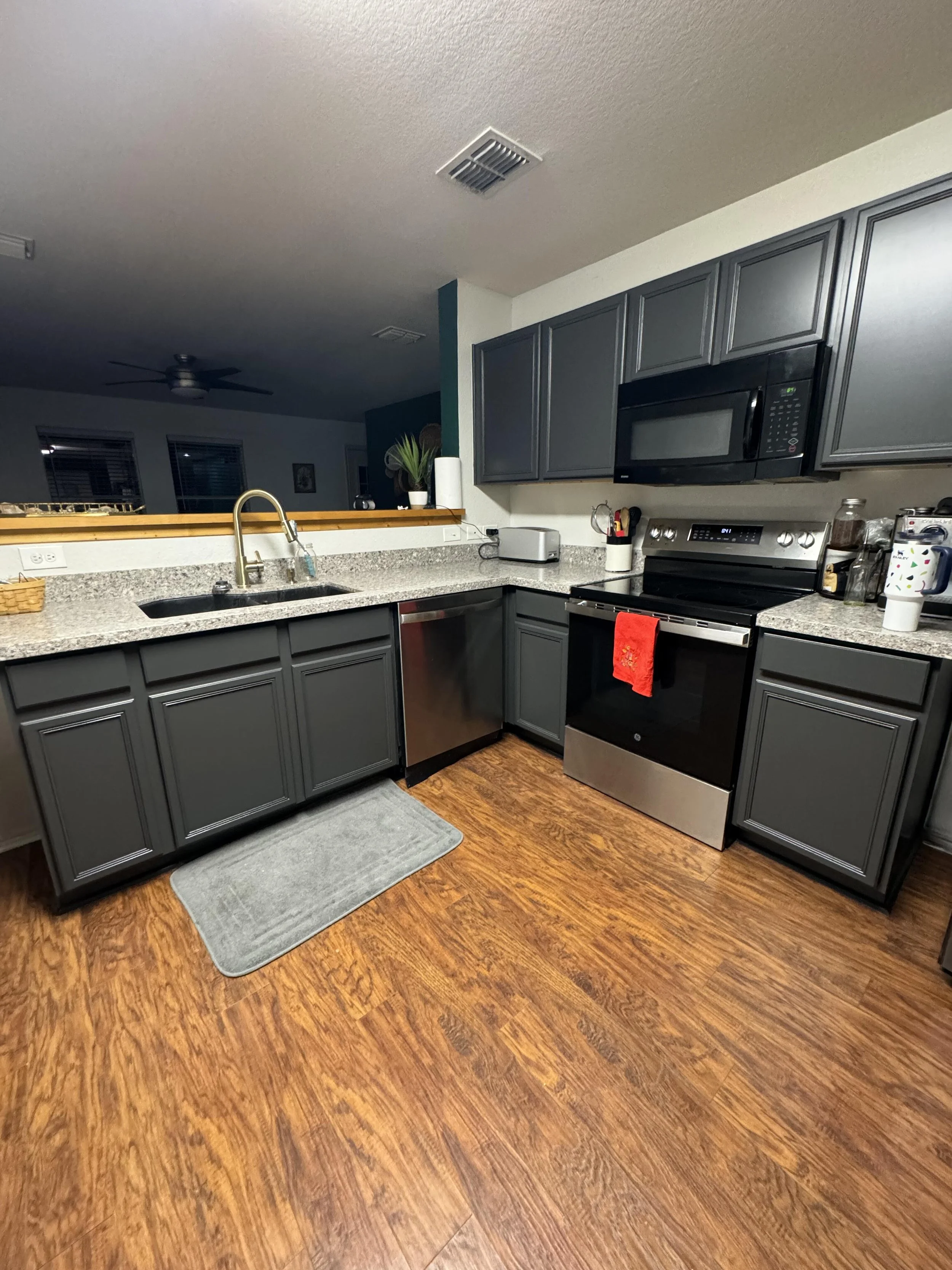 Kitchen with gray cabinets, granite countertops, black stove with red towel, microwave, dishwasher, and hardwood flooring.
